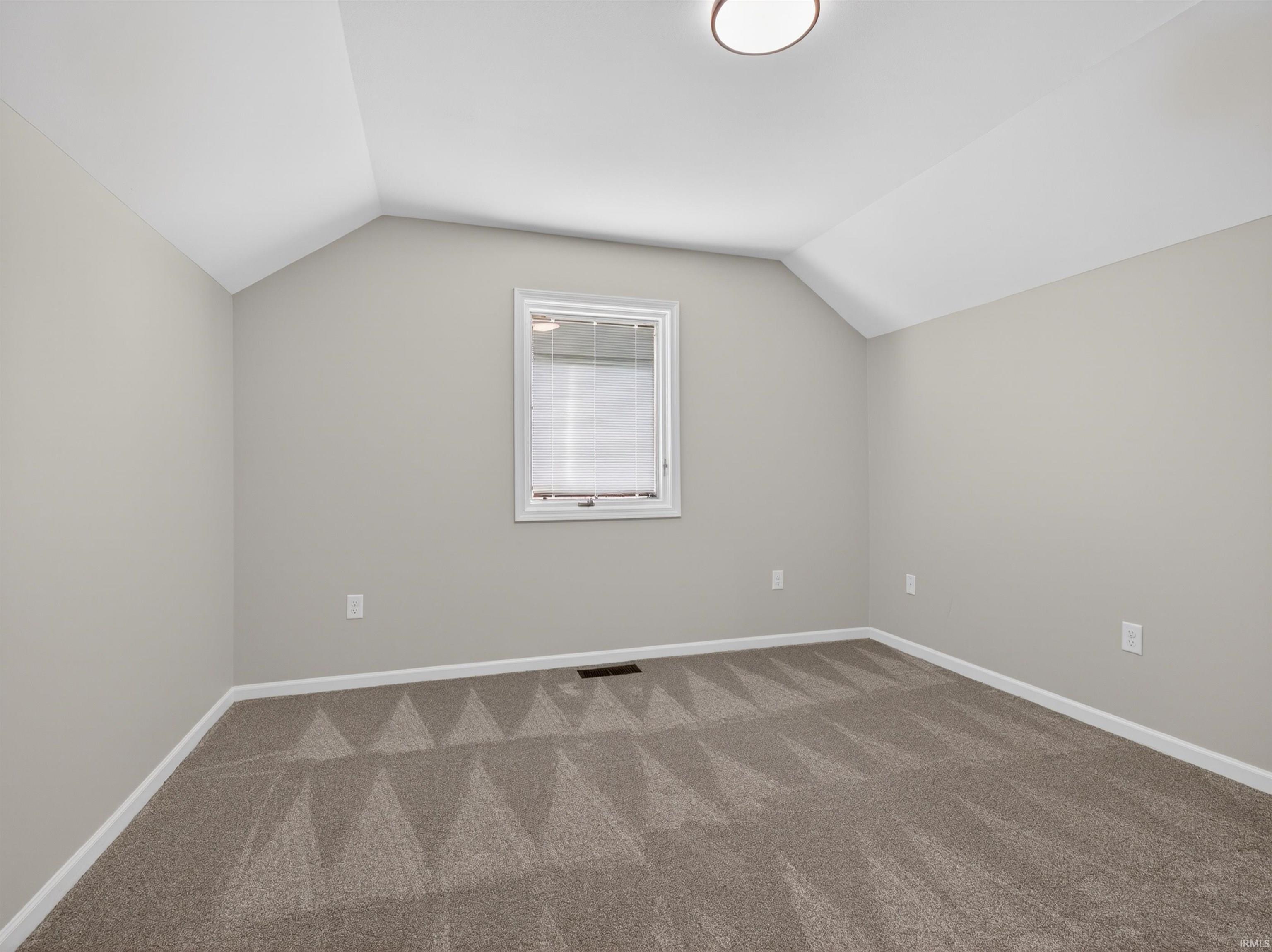 Bedroom featuring sloped ceilings, a single window with blinds, light gray wall paint, white trim, and patterned carpeting