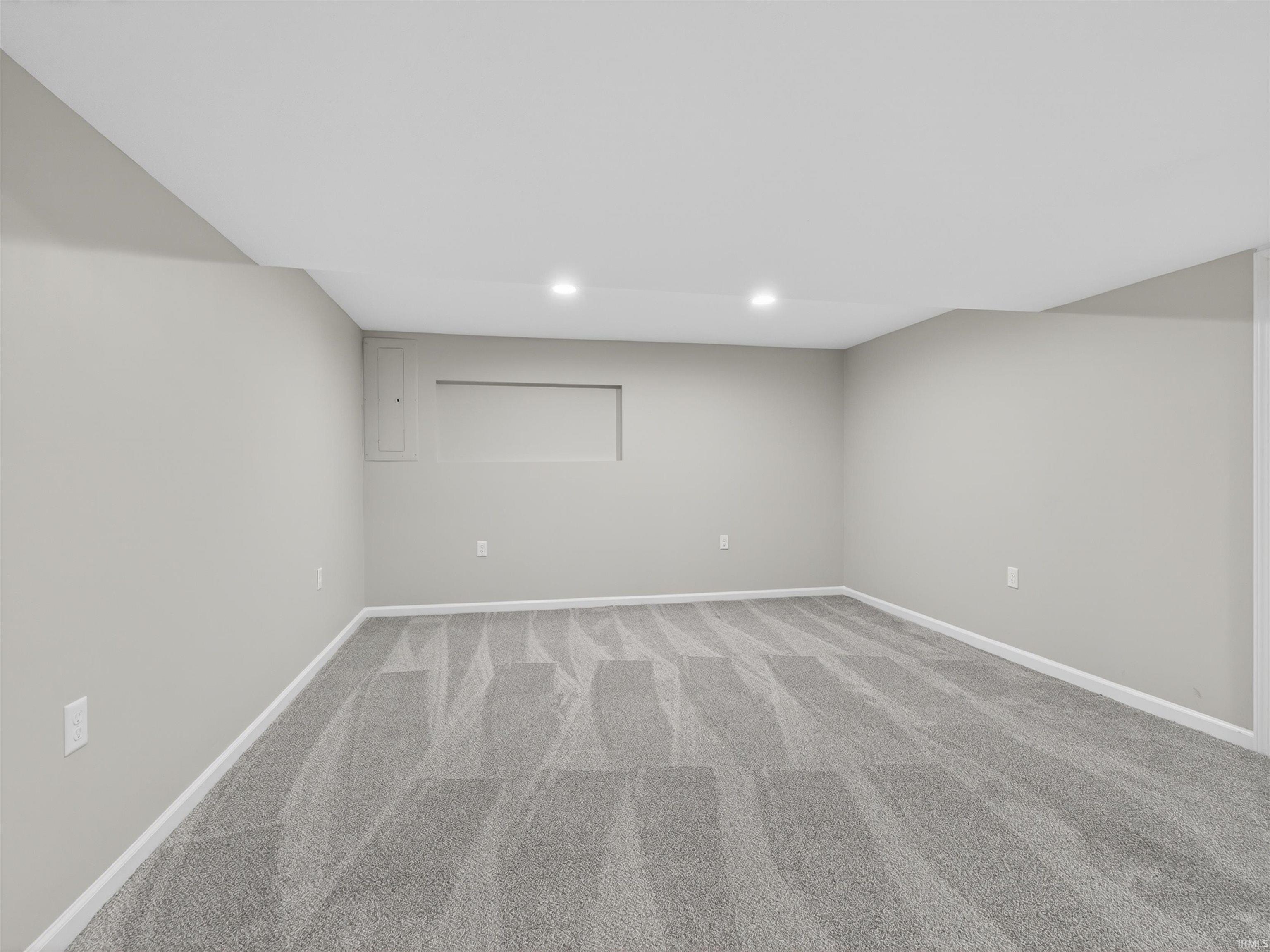 Spacious room featuring light gray walls, plush gray patterned carpeting, recessed lighting, and white baseboards