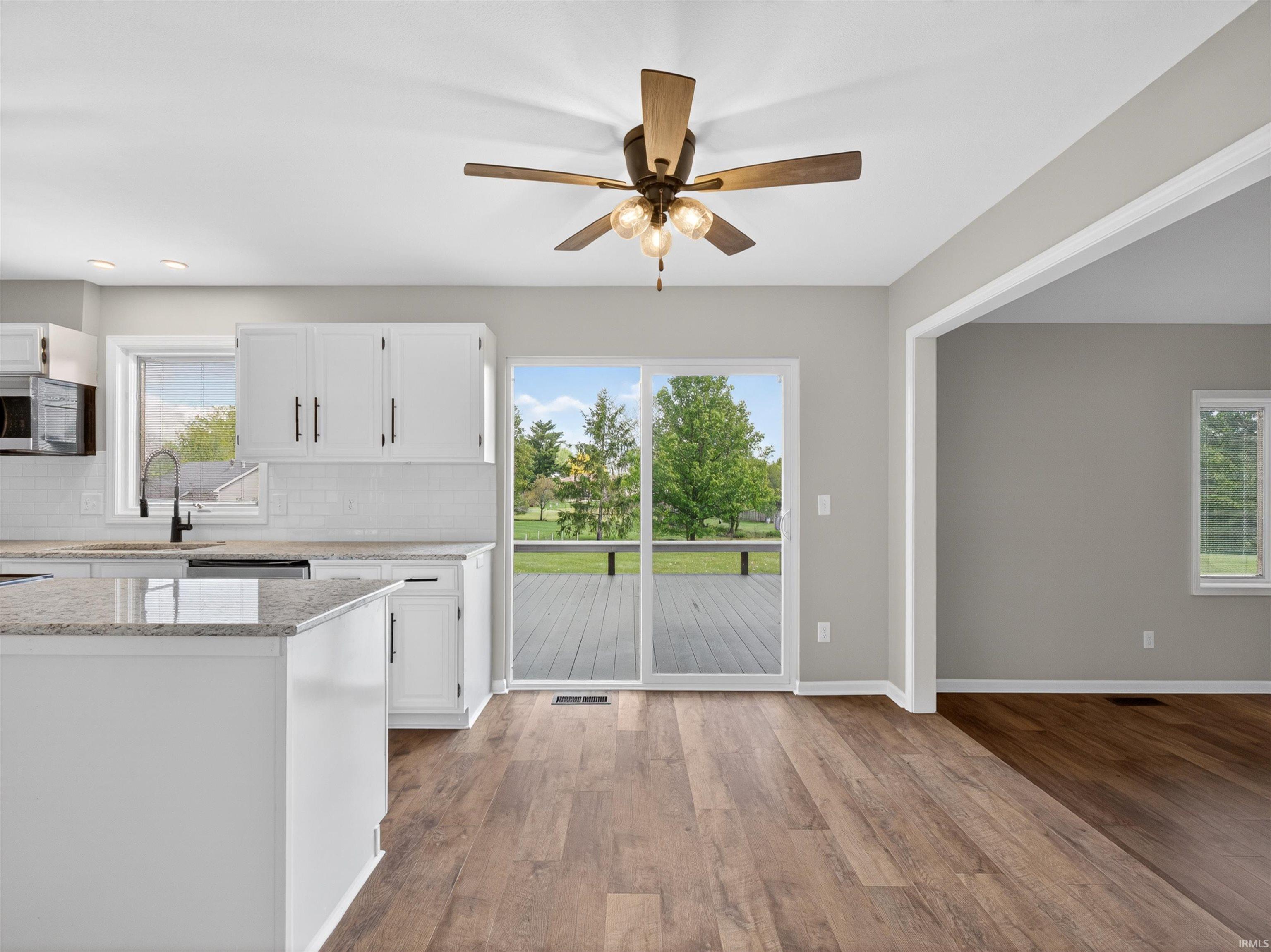 Kitchen and dining area featuring wood-finish flooring, white cabinetry with black hardware, and an island with a stone countertop