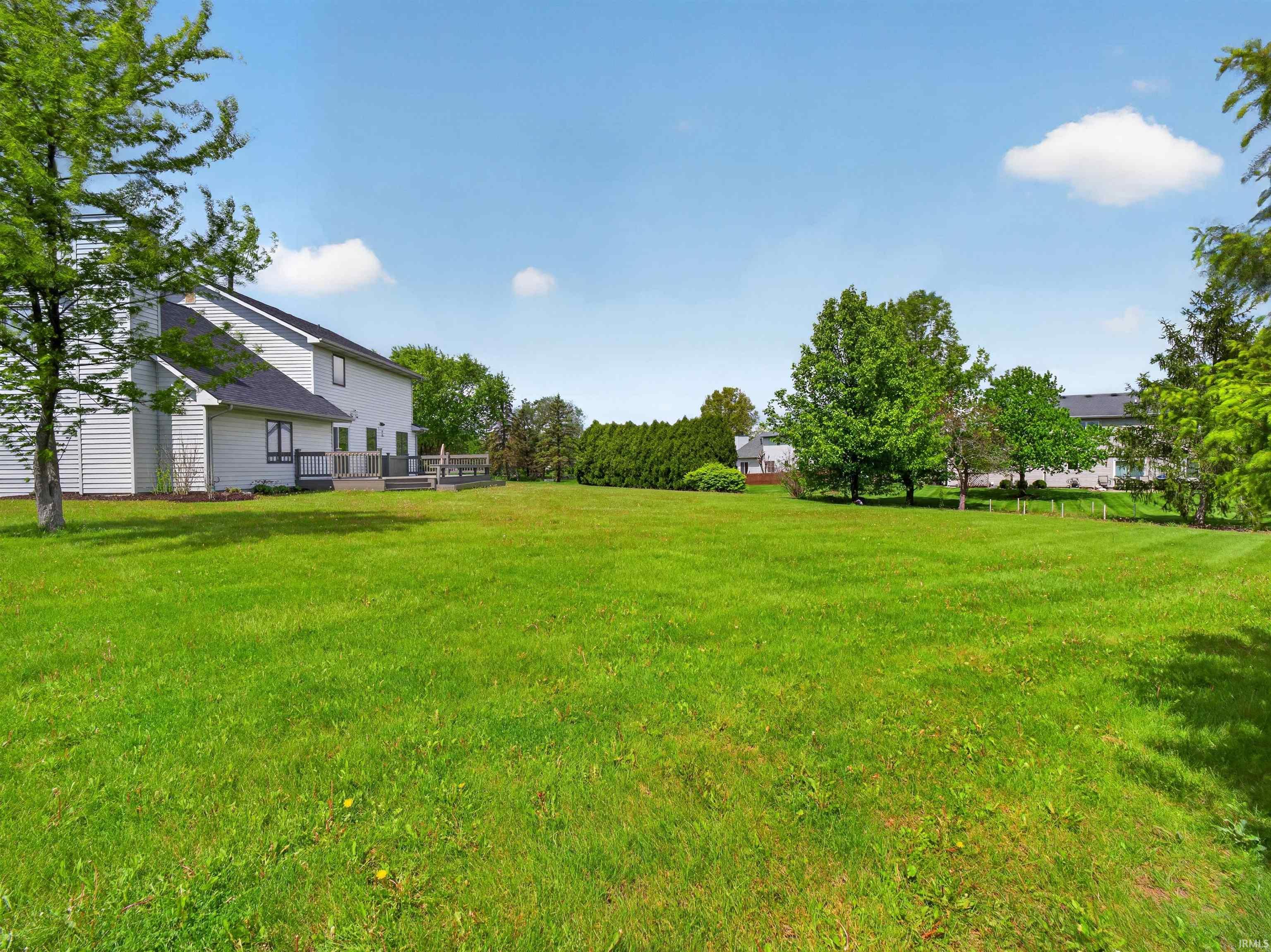 Expansive green lawn with mature trees and a multi-level wood deck