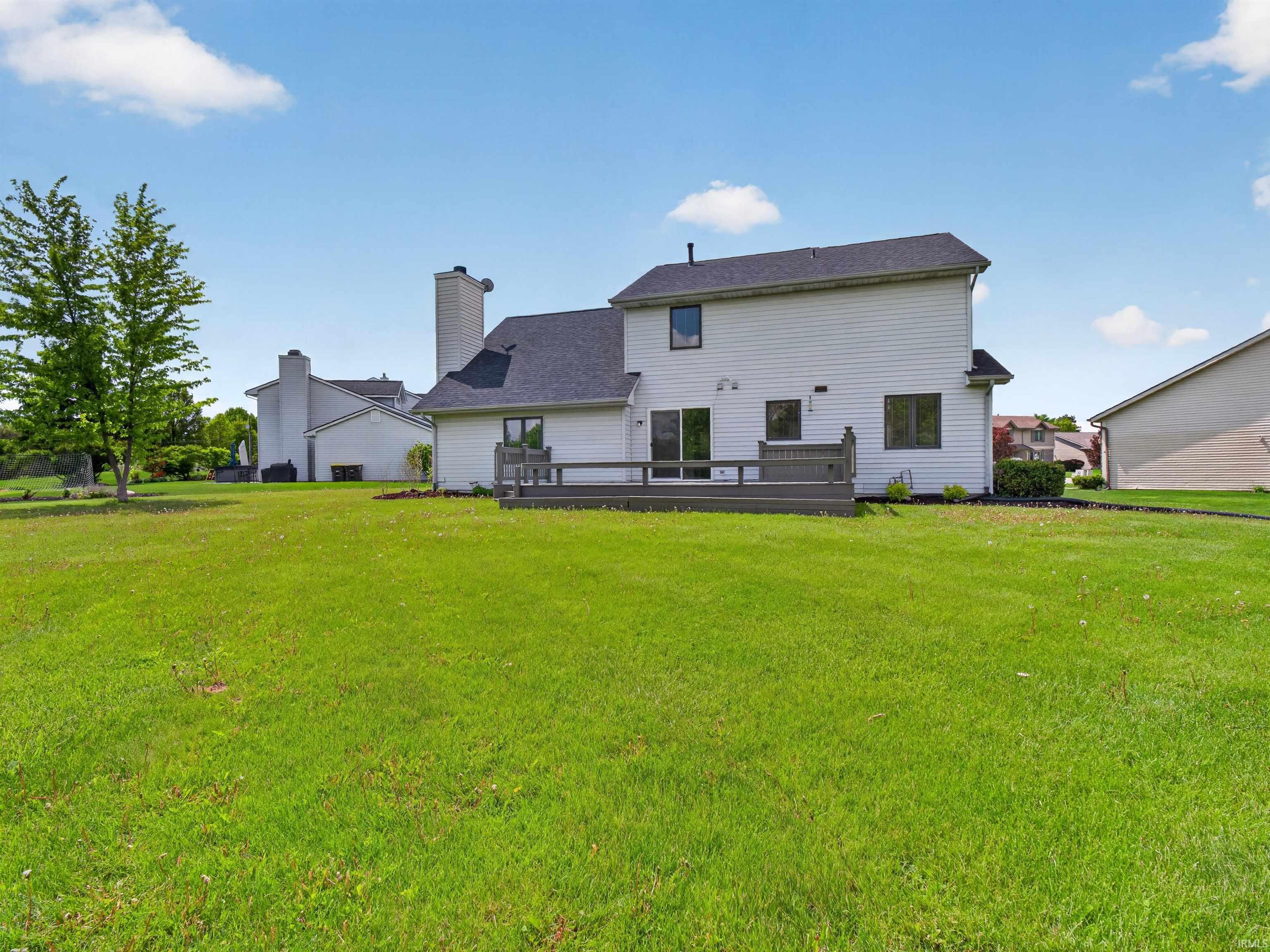 Expansive green lawn surrounds the property, featuring a multi-level deck accessible via sliding glass doors