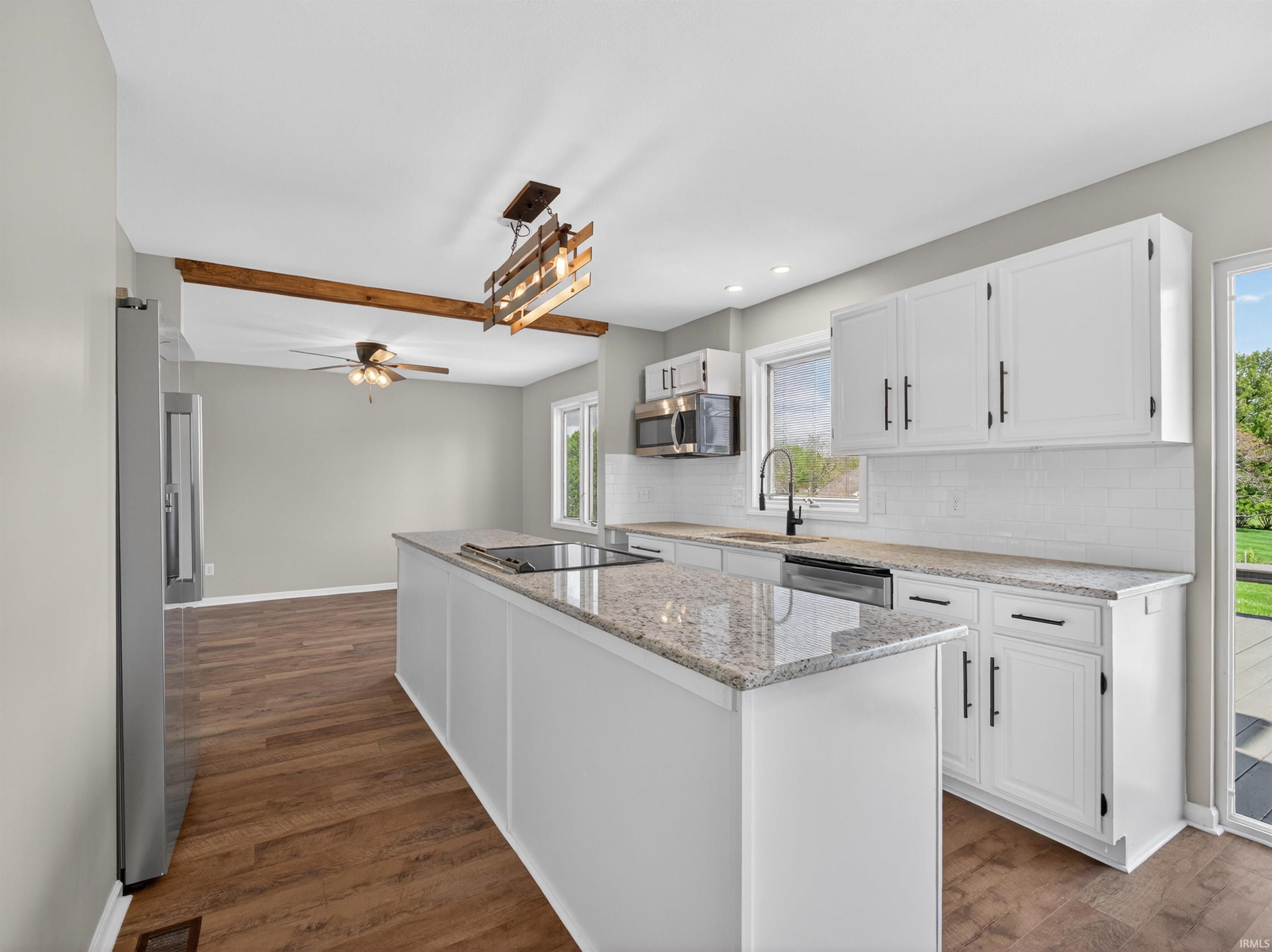 Kitchen featuring a central island with a built-in cooktop, white cabinetry with dark hardware, granite countertops, and a subway tile backsplash