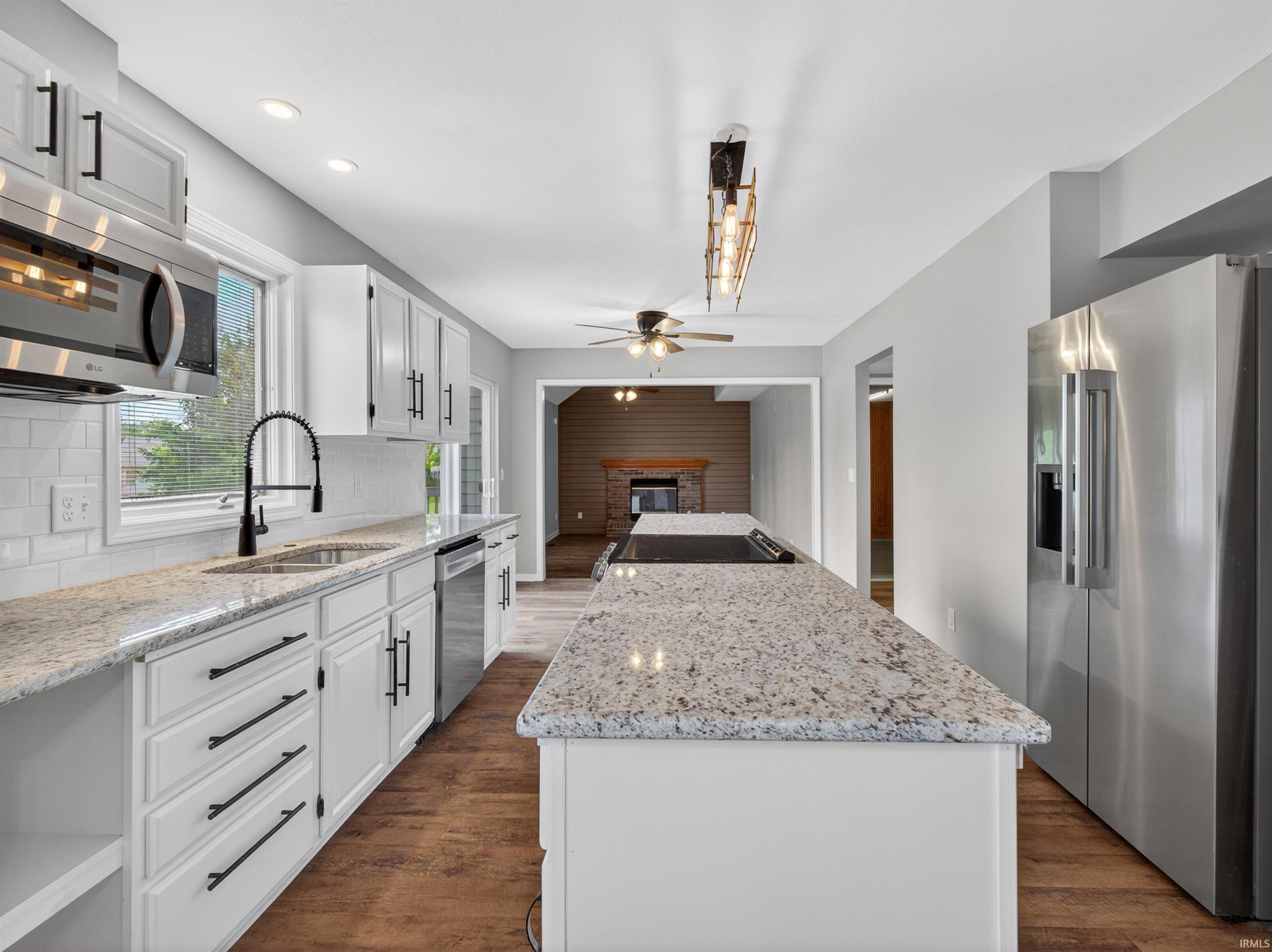 Bright kitchen featuring white cabinetry, granite countertops, stainless steel appliances, wood-finish flooring, and a subway tile backsplash