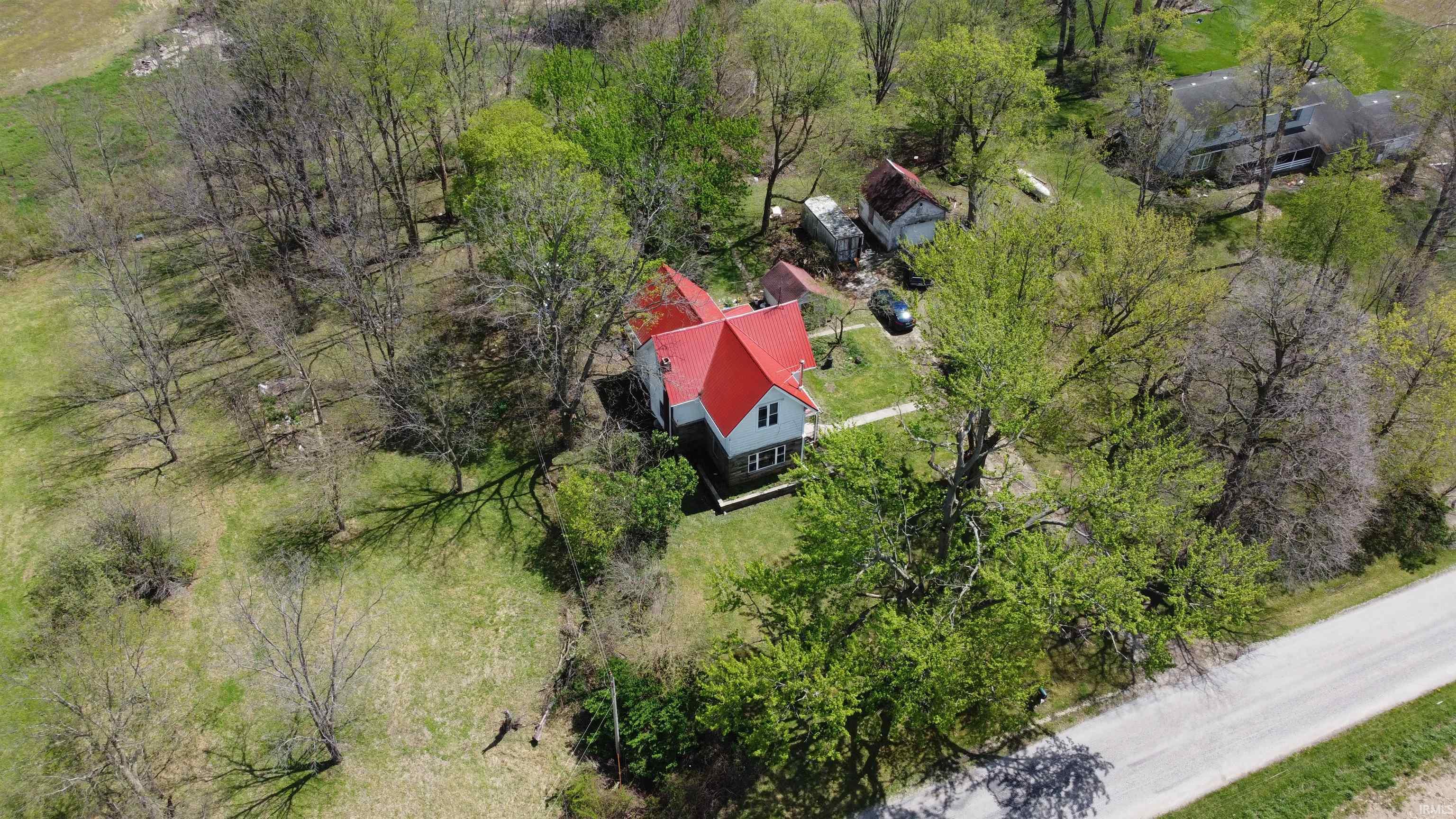 Aerial depiction of a property featuring a white residence with a red roof, surrounded by mature trees