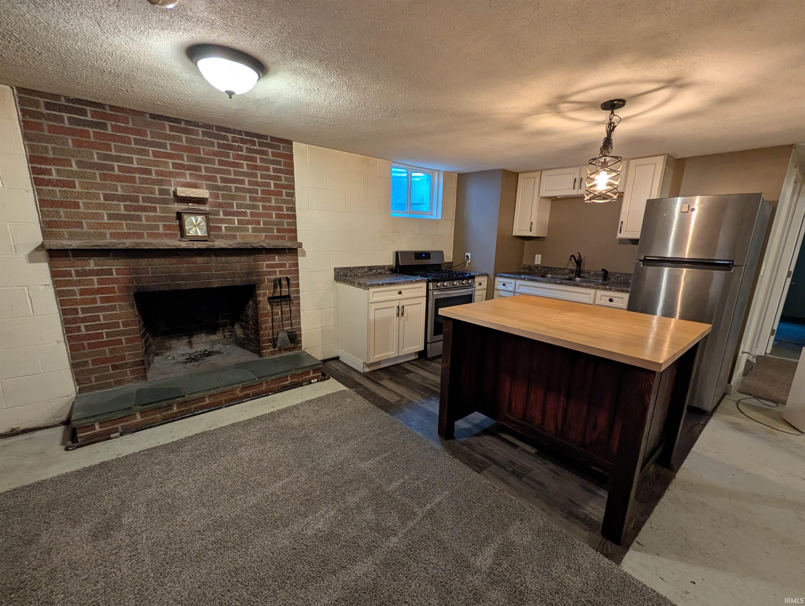 Brick fireplace with slate hearth, wood-finish flooring, white cabinetry, stainless steel appliances, and a butcher block island