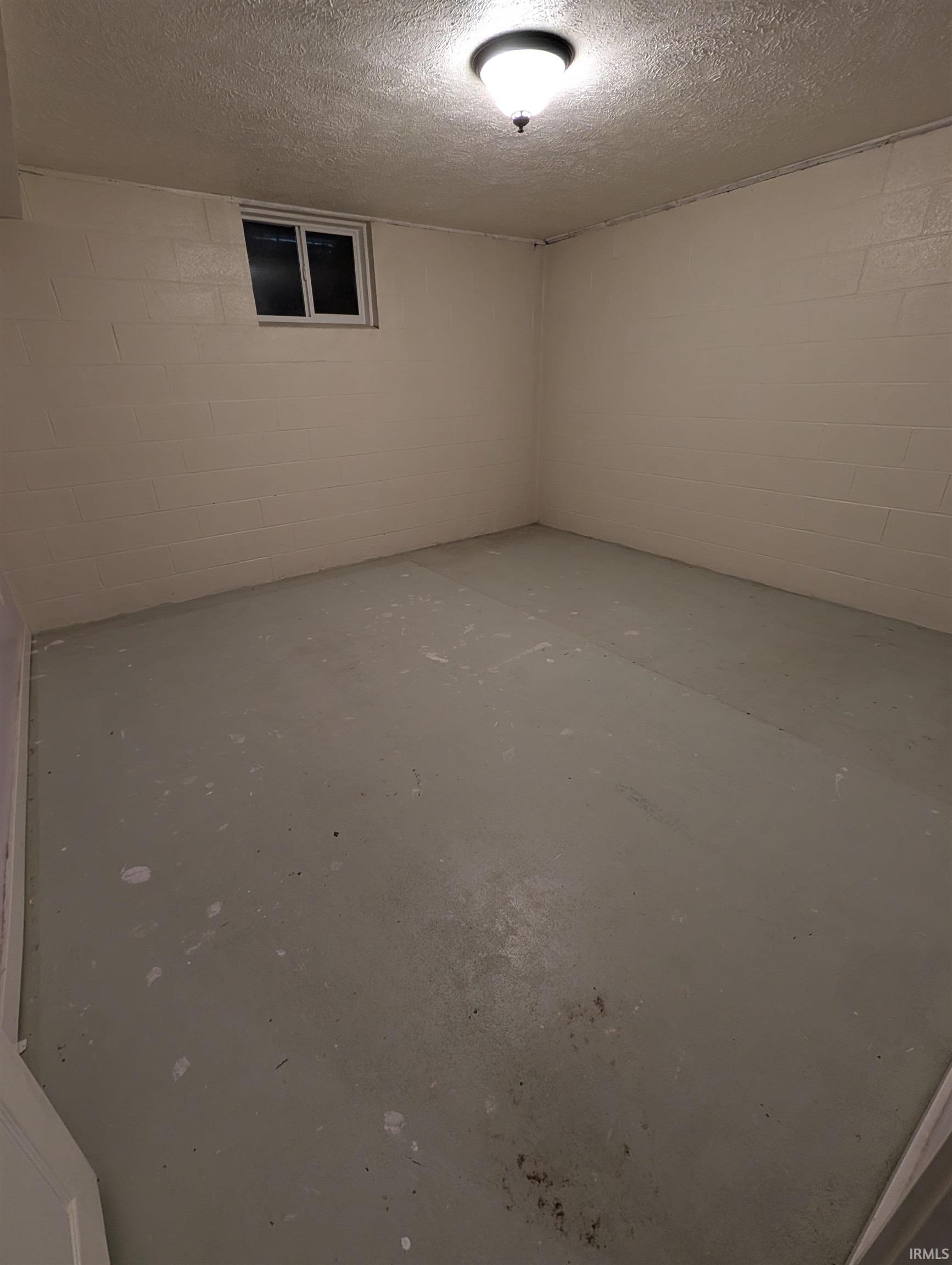 Room featuring painted concrete block walls, a single window, and a flush mount ceiling light
