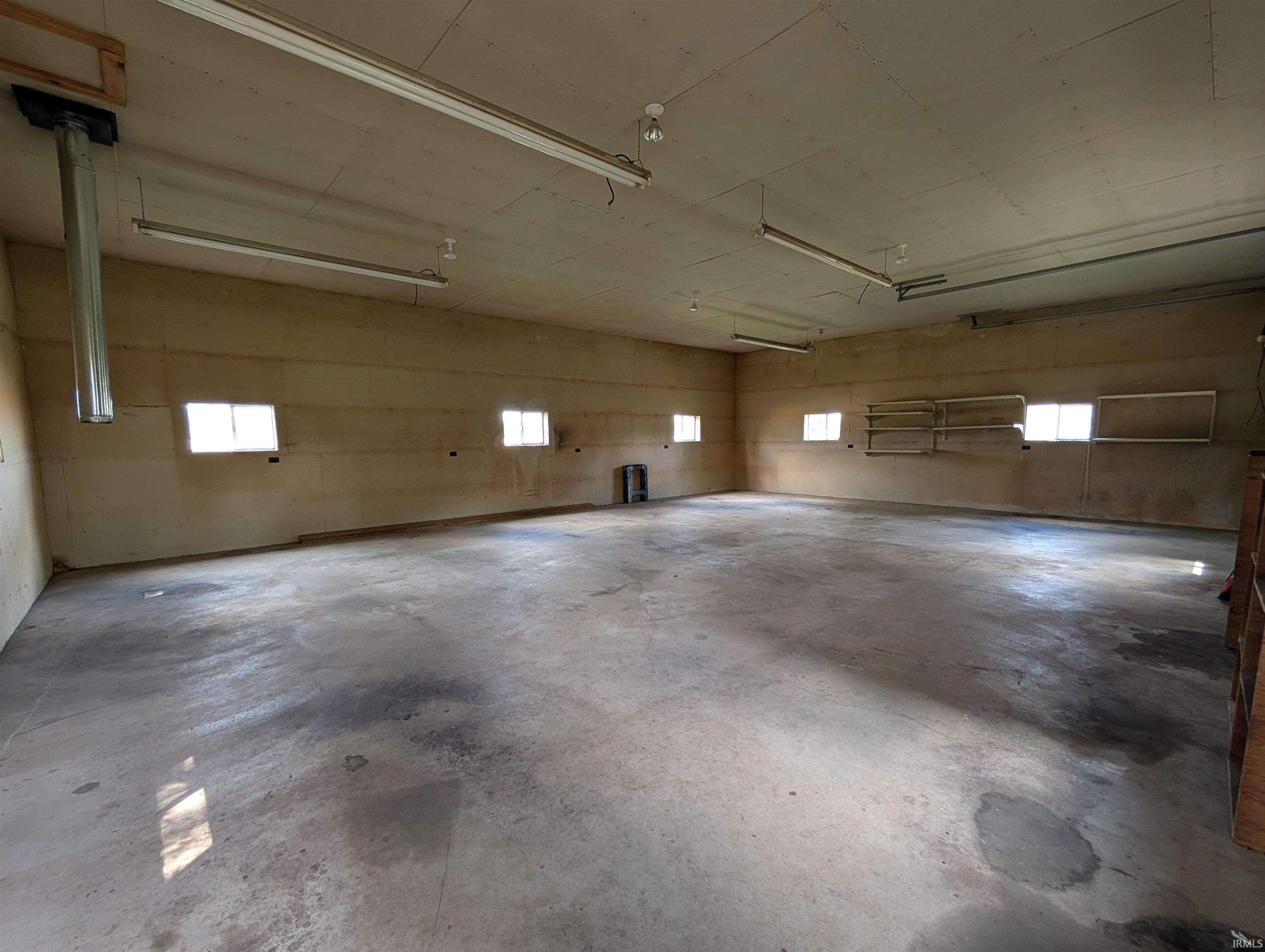 Spacious interior featuring a concrete floor, multiple windows, and overhead fluorescent lighting