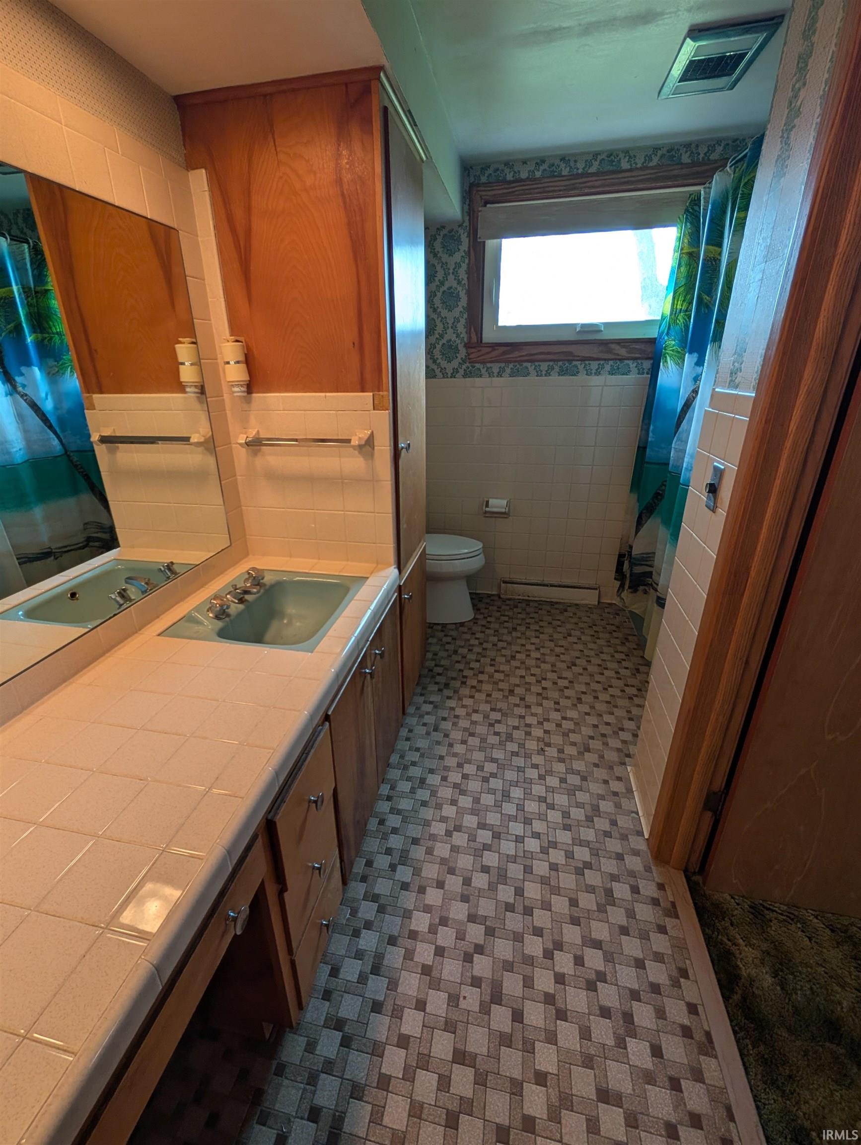 Bathroom featuring an extended vanity with tile countertop, dual integrated sinks, and wood-finish cabinetry