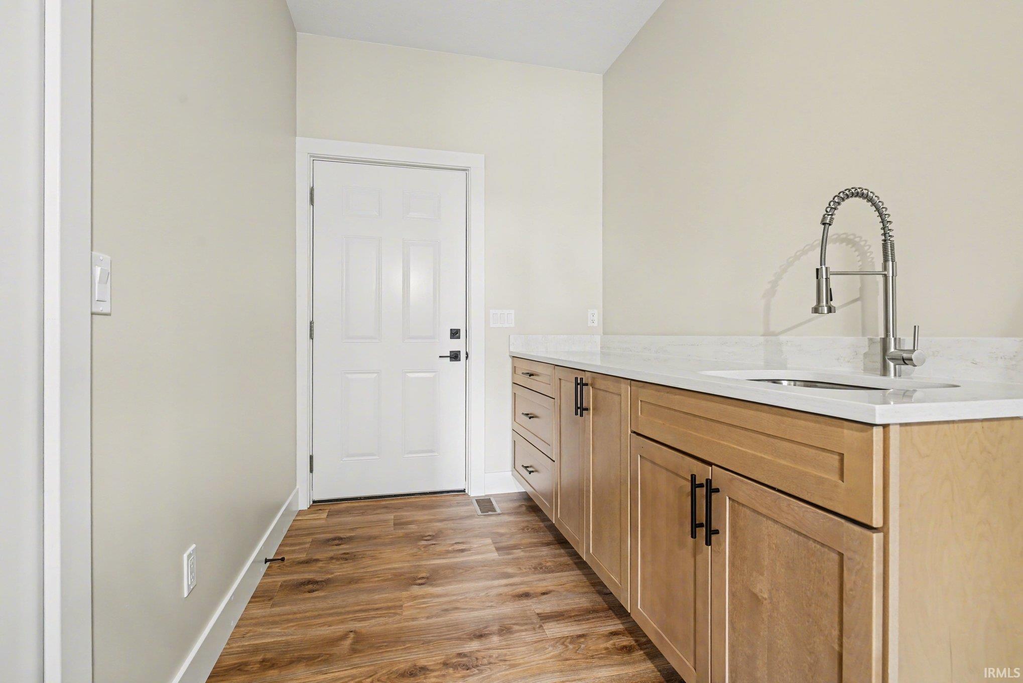 Light wood-finish cabinetry with matte black hardware, a stainless steel sink, and a high-arc faucet