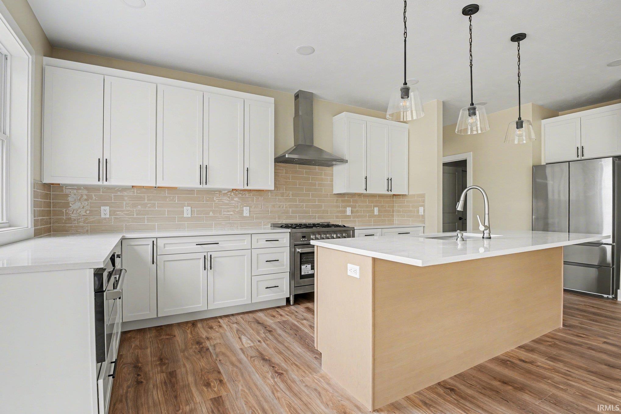 Kitchen featuring a central island with a sink, white cabinetry, stainless steel appliances, wood-finish flooring, and subway tile backsplash