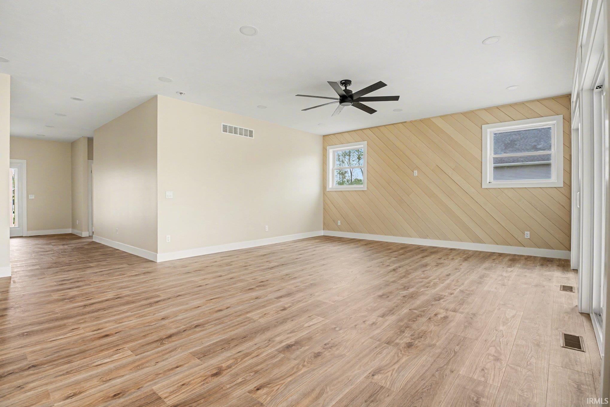 Open concept space featuring wood-finish flooring, a contemporary ceiling fan, and a focal wall with diagonal wood paneling
