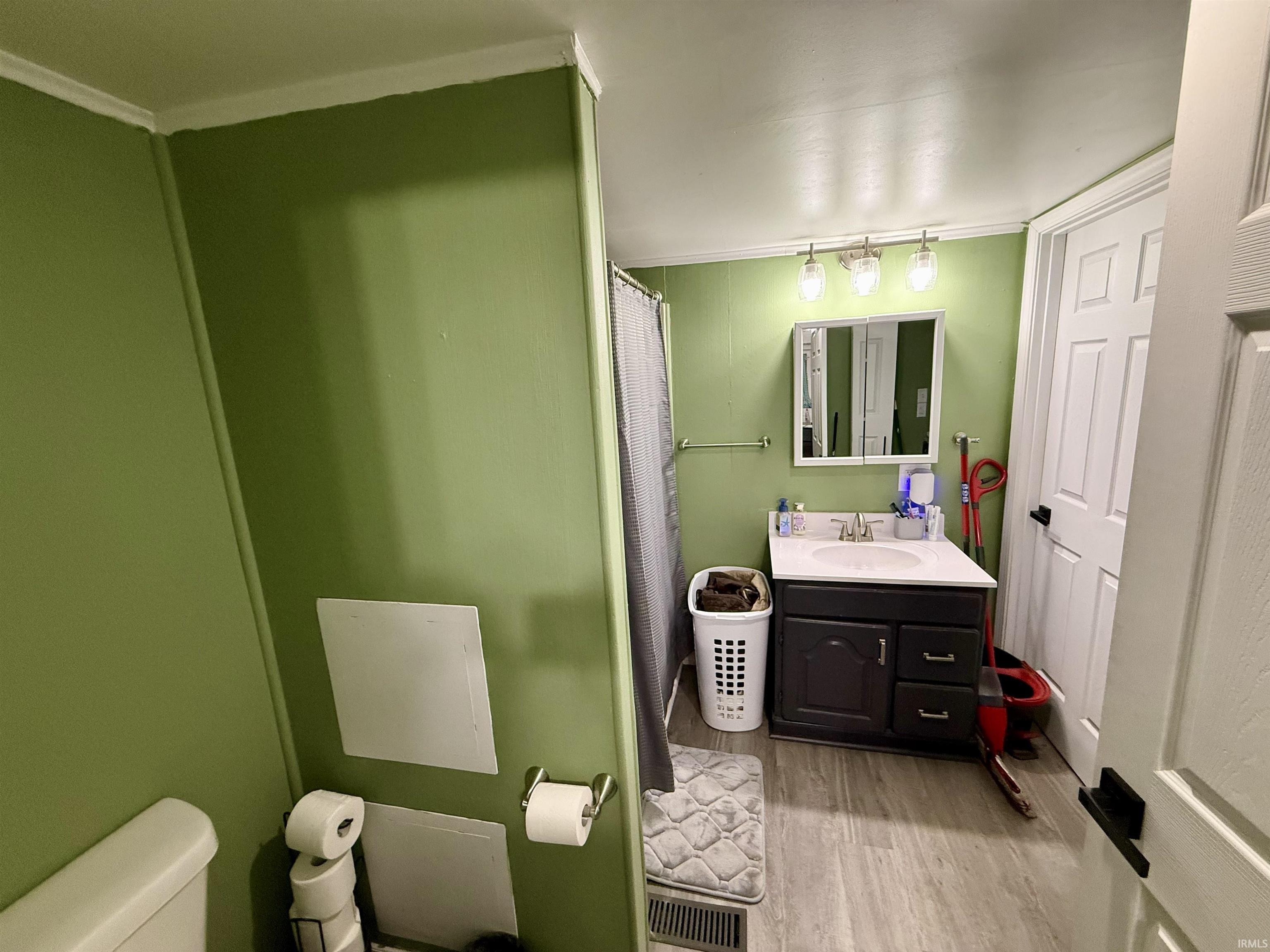 Bathroom featuring a dark wood-finish vanity with an white sink, a multi-paneled medicine cabinet, and a three-light fixture
