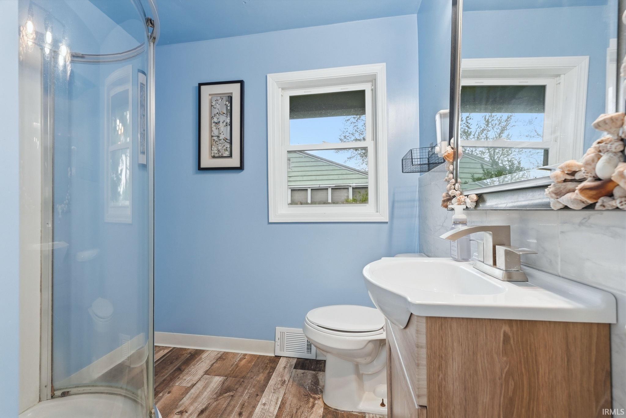Bathroom featuring a curved glass shower enclosure, wood-finish flooring, and a single-pane window