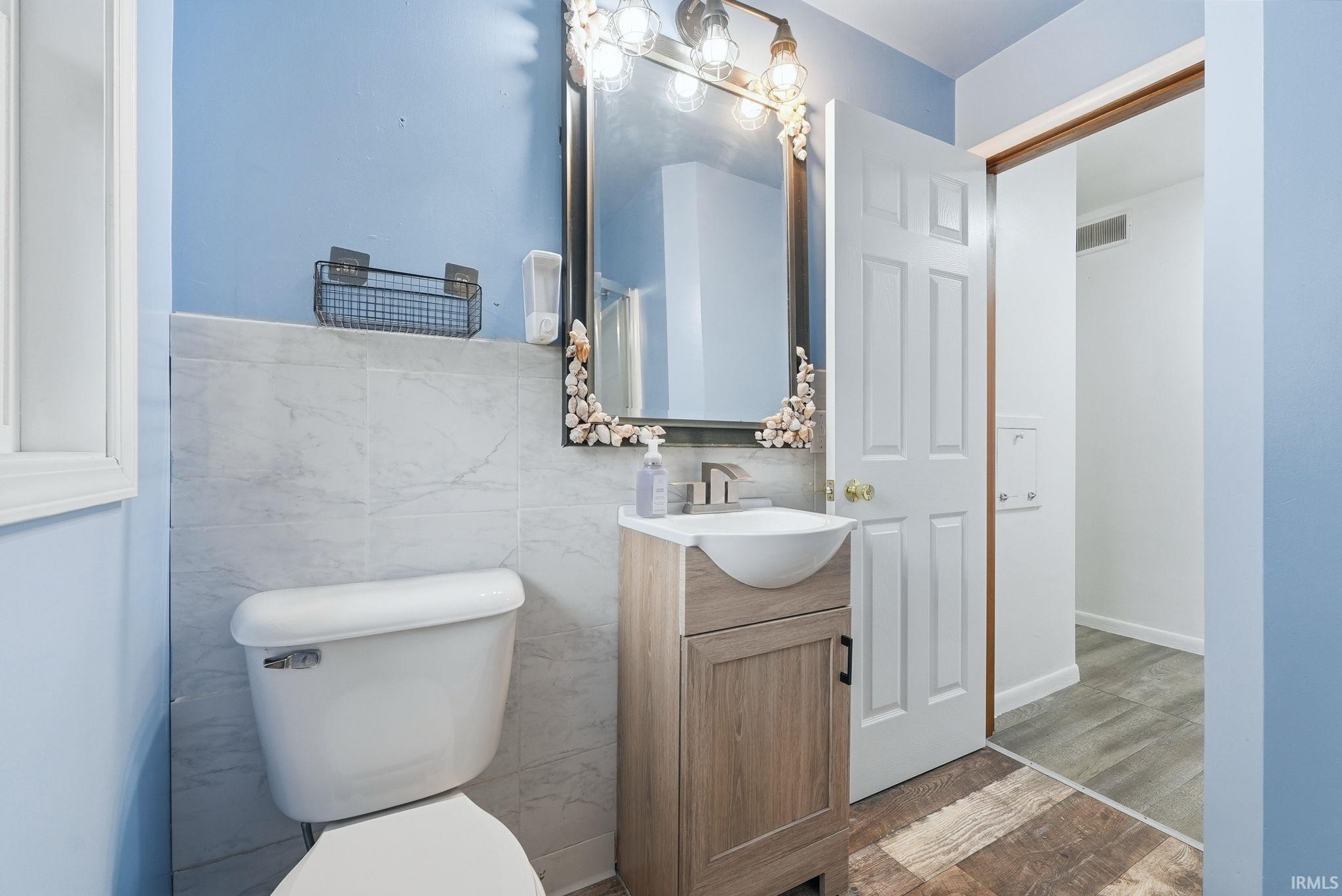 Bathroom featuring a light blue wall color, white rectangular wall tiles, a wood-finish vanity with a vessel sink, and an overhead vanity light fixture