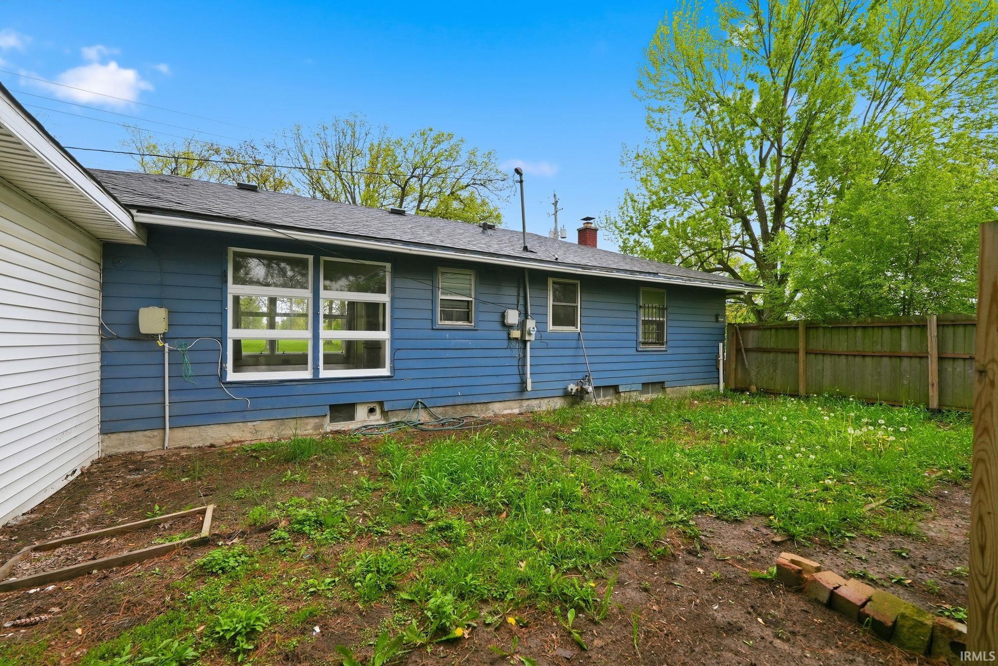 Spacious rear yard featuring a partial wood fence, mature perimeter trees, and a blue-sided exterior with white trim