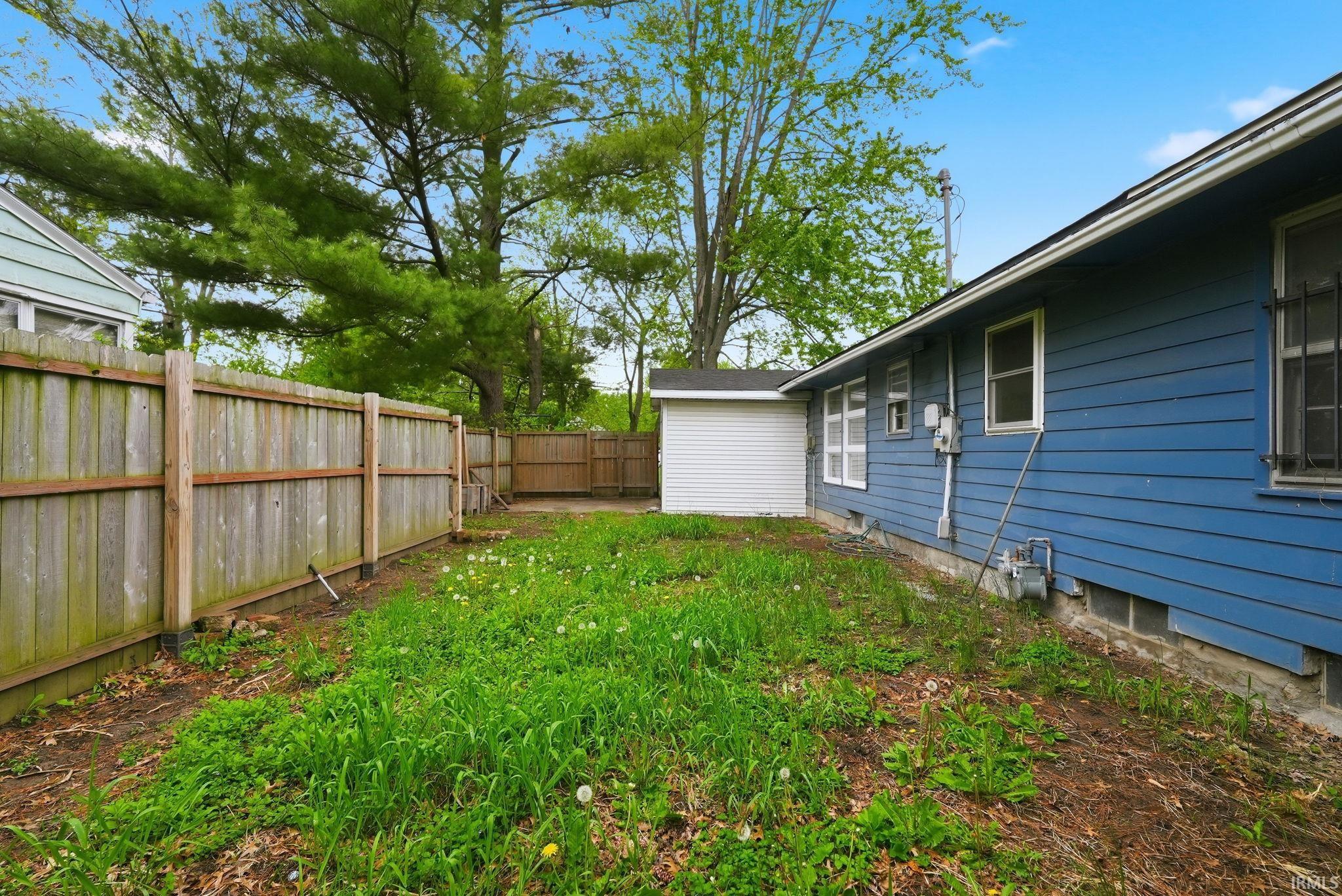 Side yard featuring a wood fence, detached white siding shed, and blue horizontal siding