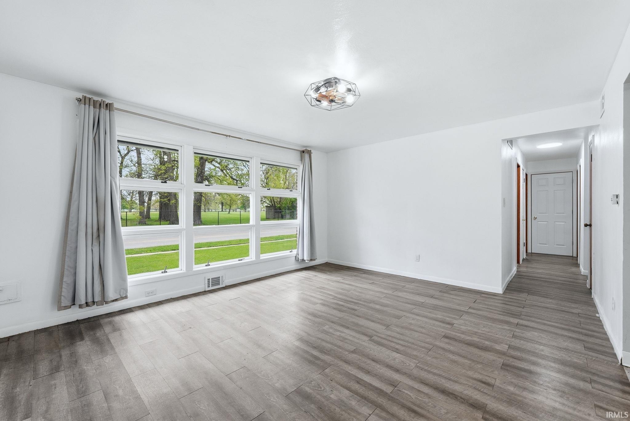 Spacious living area featuring expansive windows, wood-finish flooring, white walls, a flush-mount light fixture, and a hallway with paneled doors