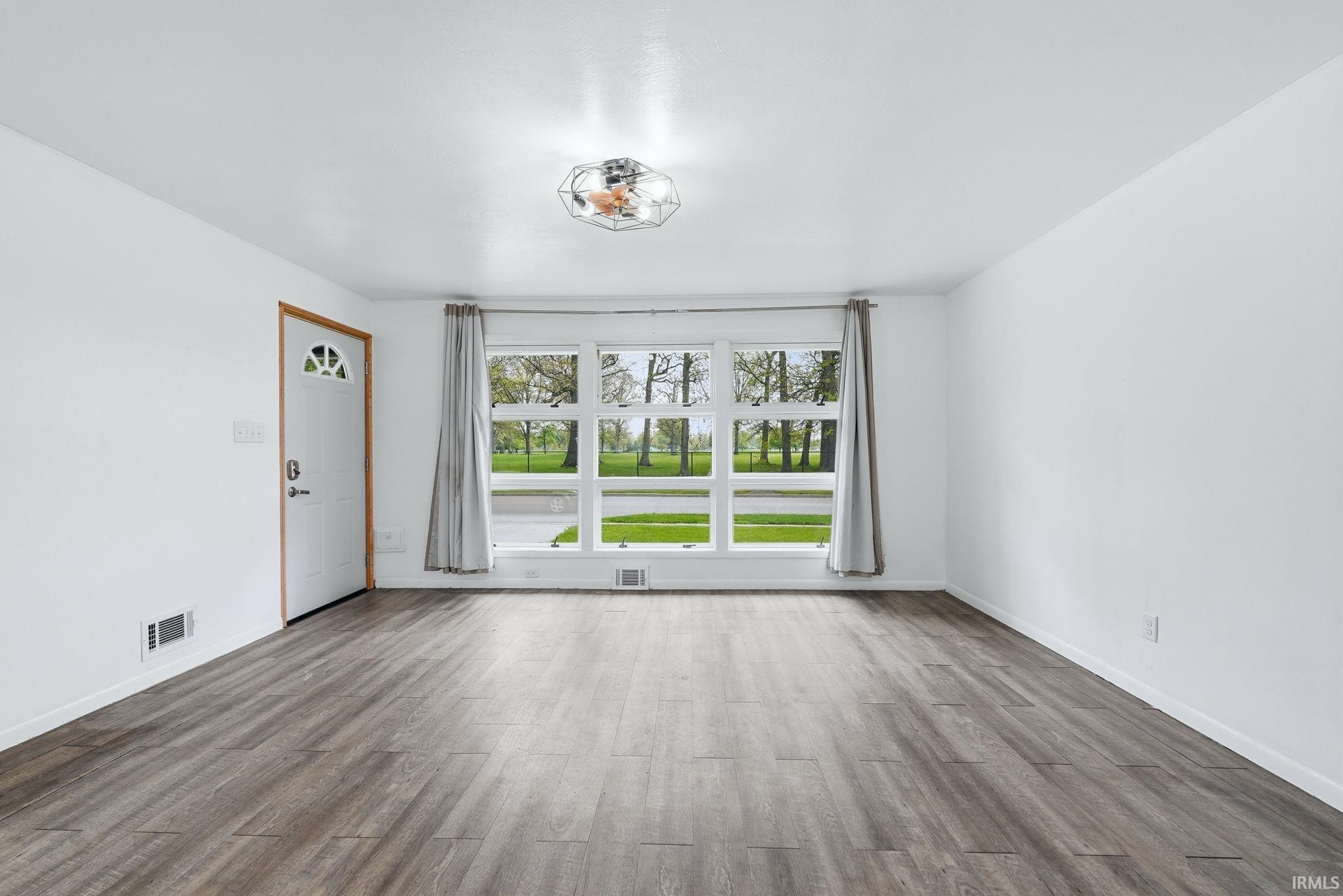 Spacious room featuring wood-finish flooring, white walls, and a large window with a natural landscape