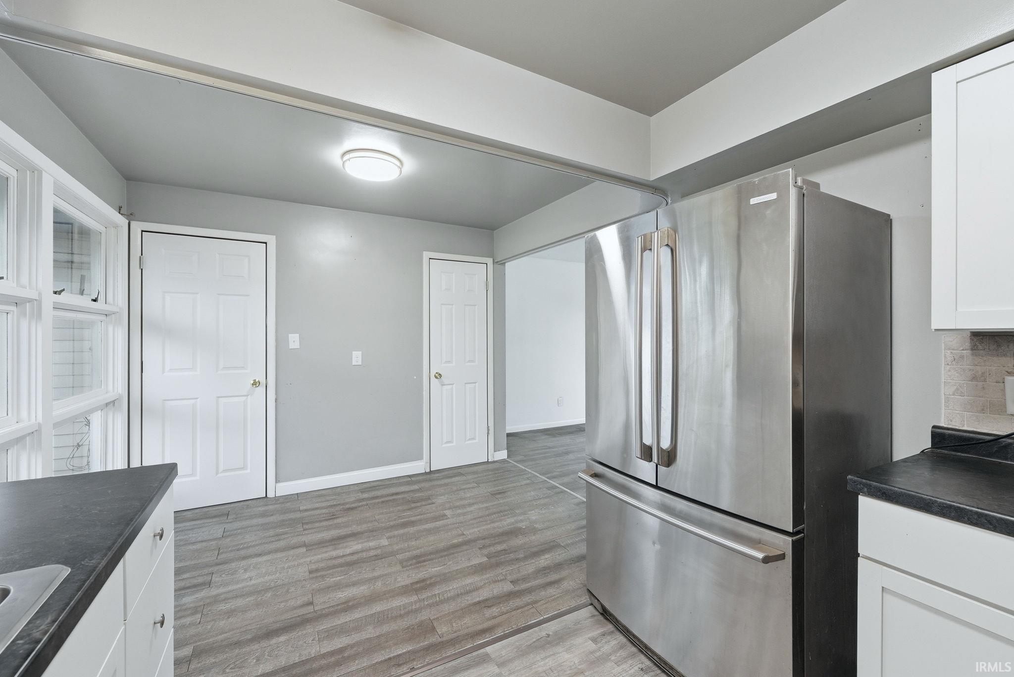 Modern kitchen featuring wood-finish flooring, white cabinetry, dark countertops, and a stainless steel refrigerator