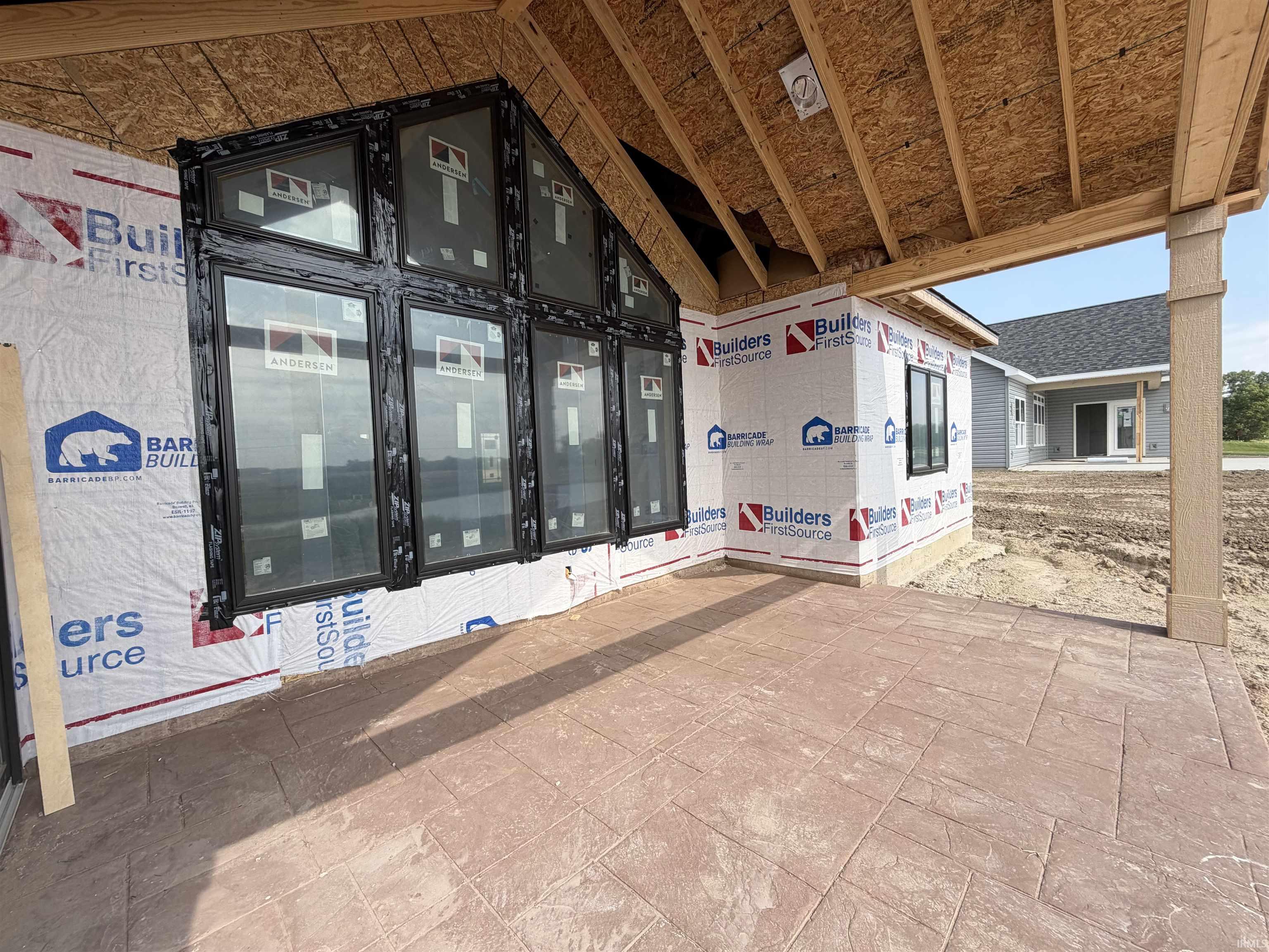 Covered patio featuring an imprinted concrete surface, an exposed timber ceiling, and a prominent window array with black frames