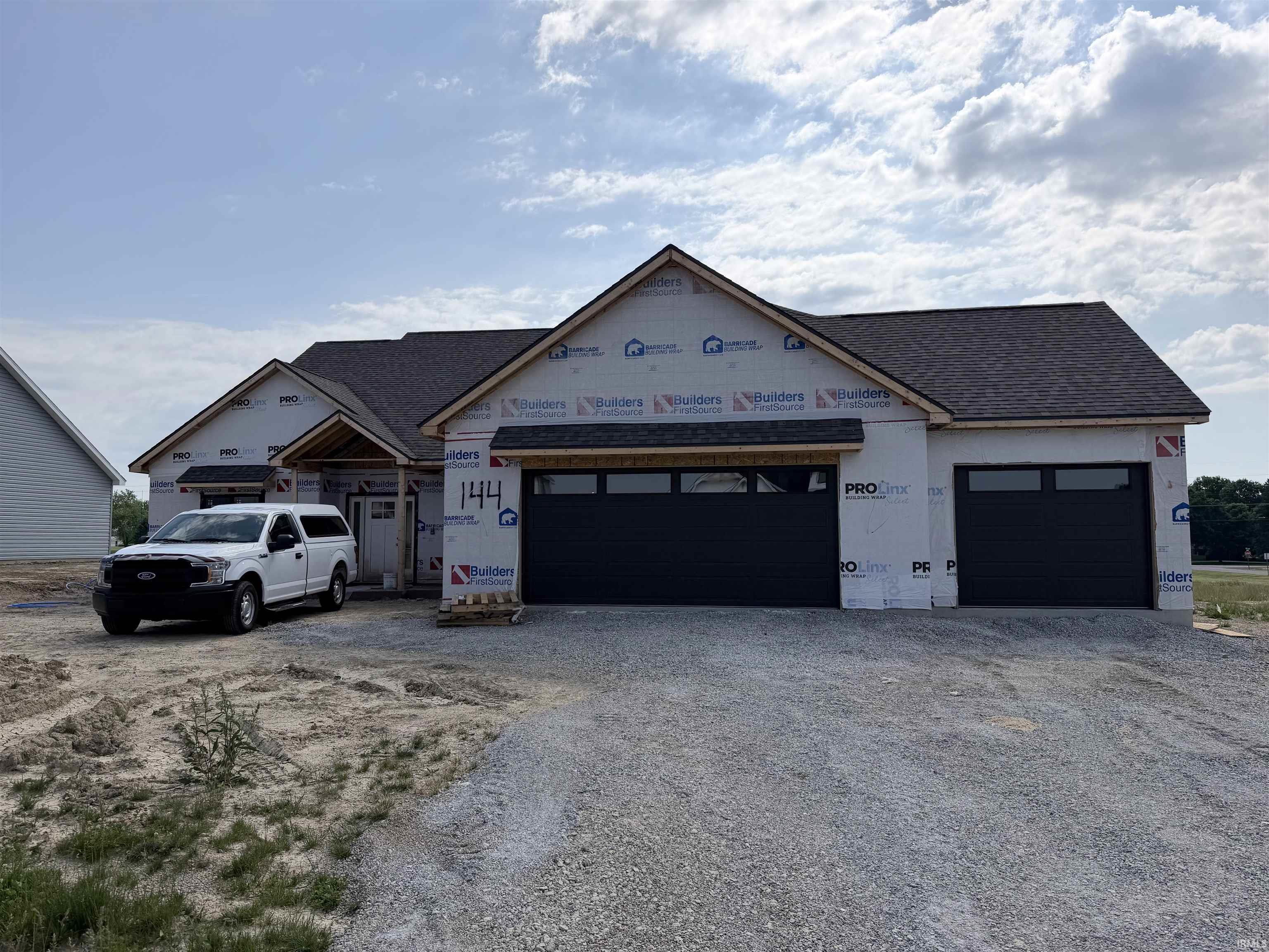 Newly constructed home featuring a dark shingled roof, two-car garage with black doors and window inserts, and an inviting covered entry