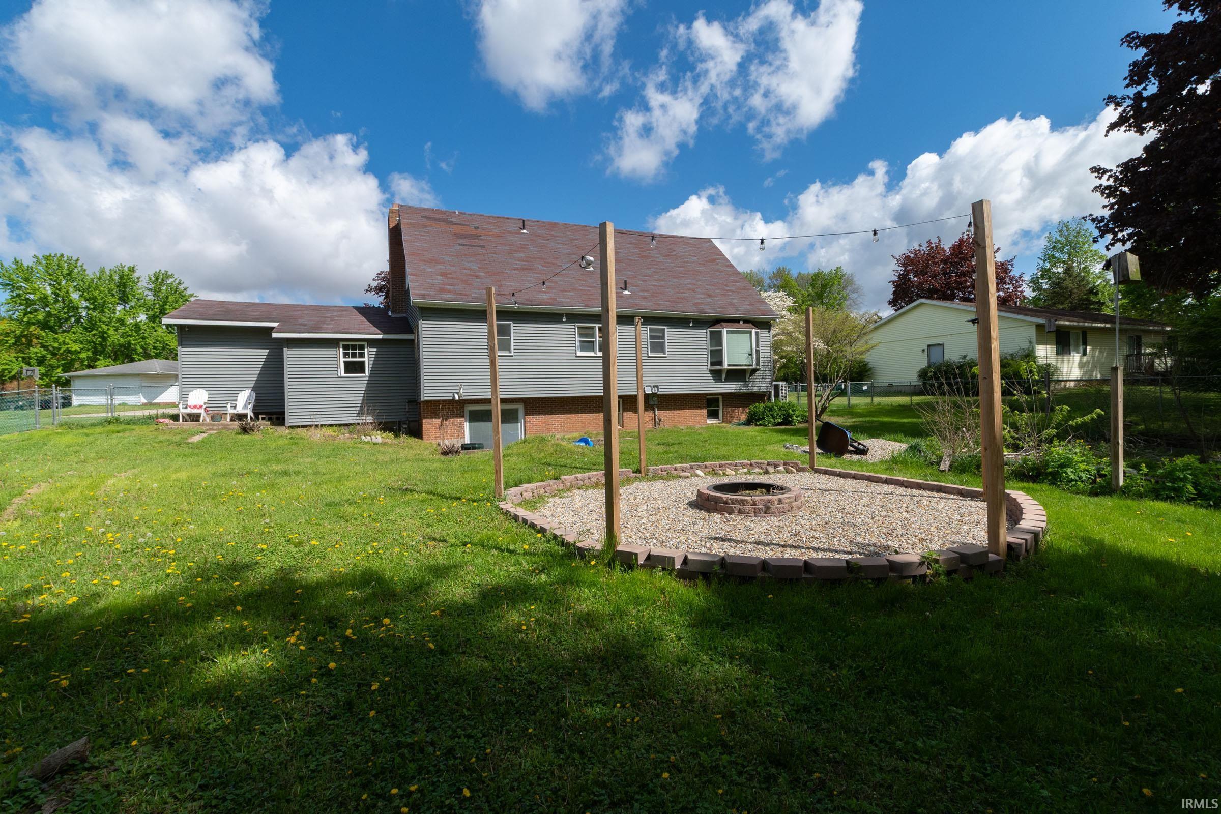 Expansive backyard featuring a gravel fire pit area with a brick border, multiple mature trees, and a detached garage in the distance