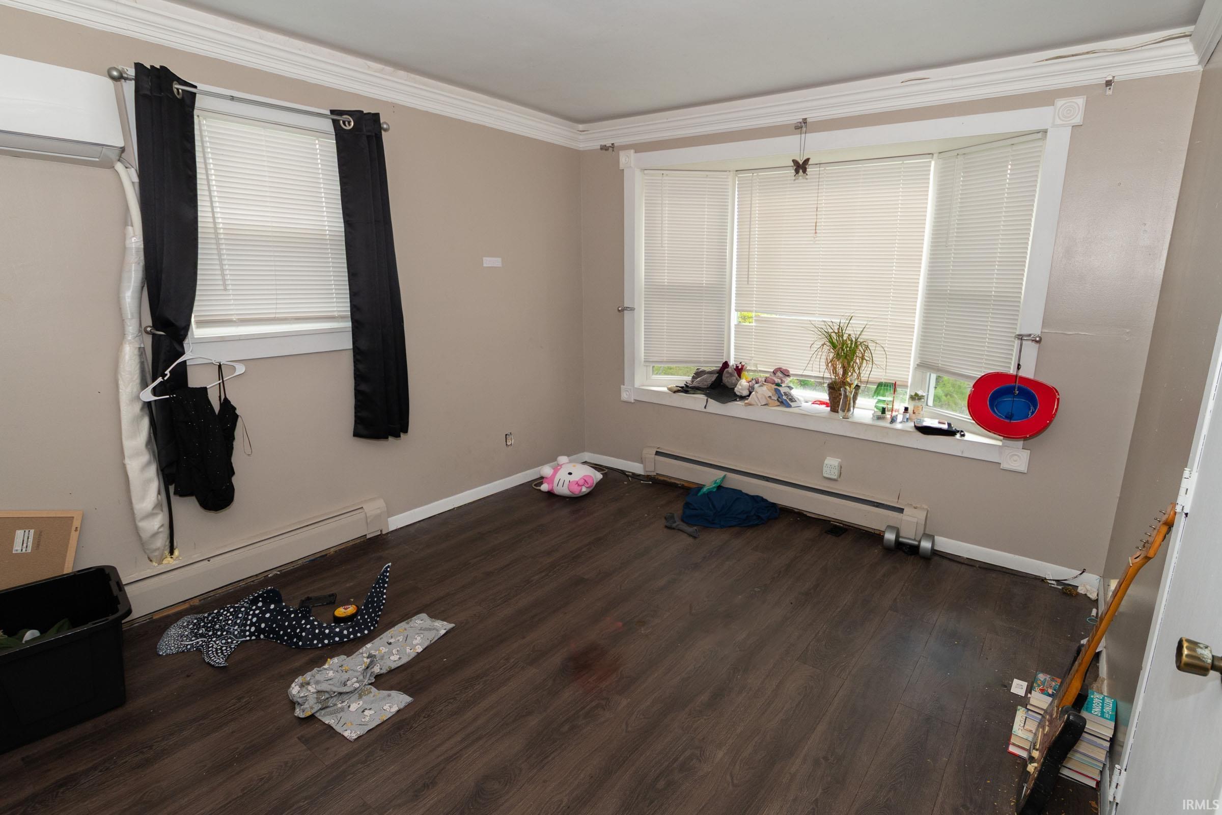 Interior room featuring dark wood-finish flooring, light tan walls, and white crown molding