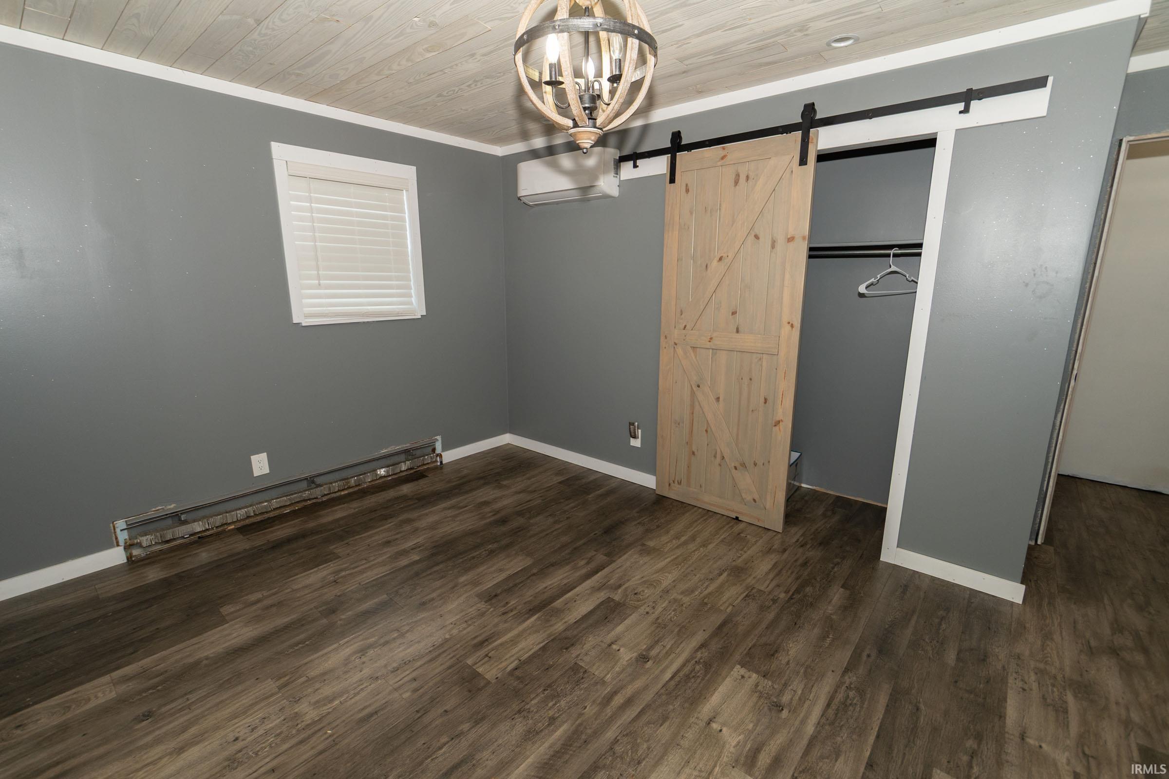 Spacious room featuring wood-finish flooring, a barn door, a wood-paneled ceiling, a ceiling light fixture, and a mini-split heating and cooling unit