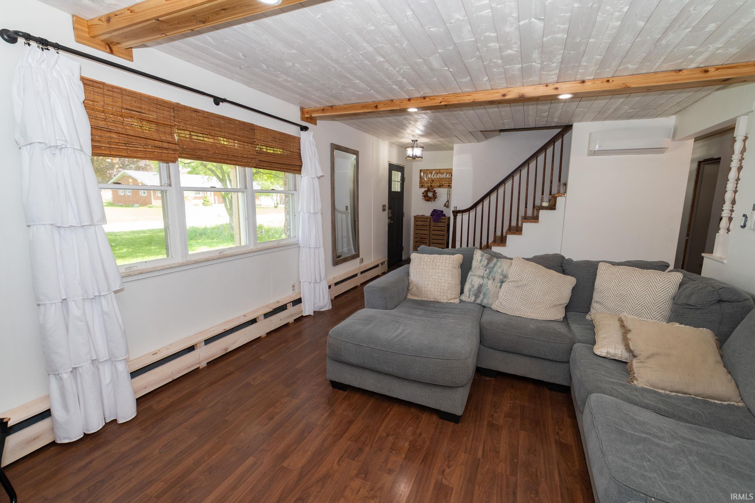 Living area featuring wood-finish flooring, a white planked ceiling with exposed wood beams, and recessed lighting
