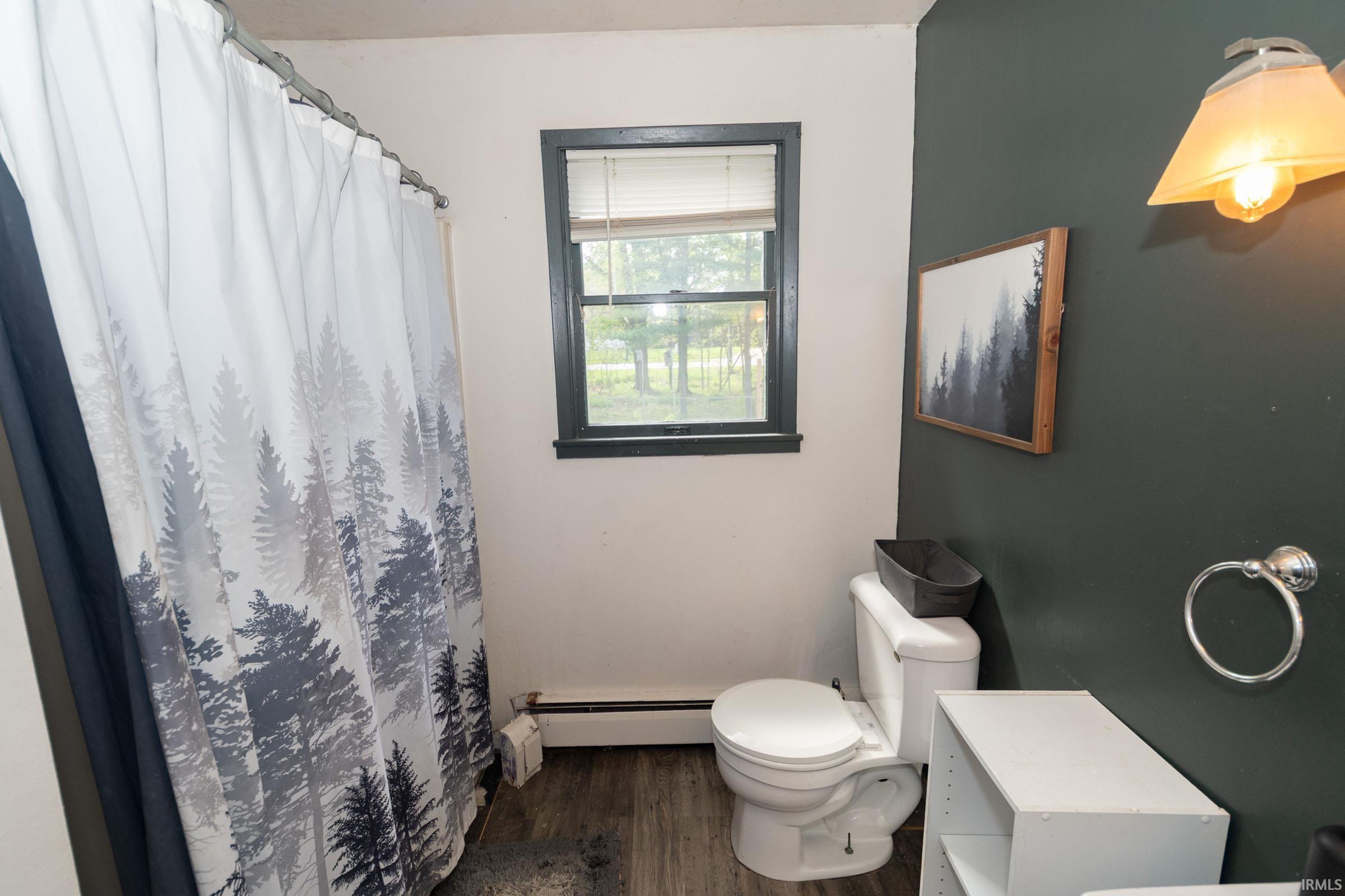 Bathroom featuring wood-finish flooring, a white toilet, and a window with dark trim
