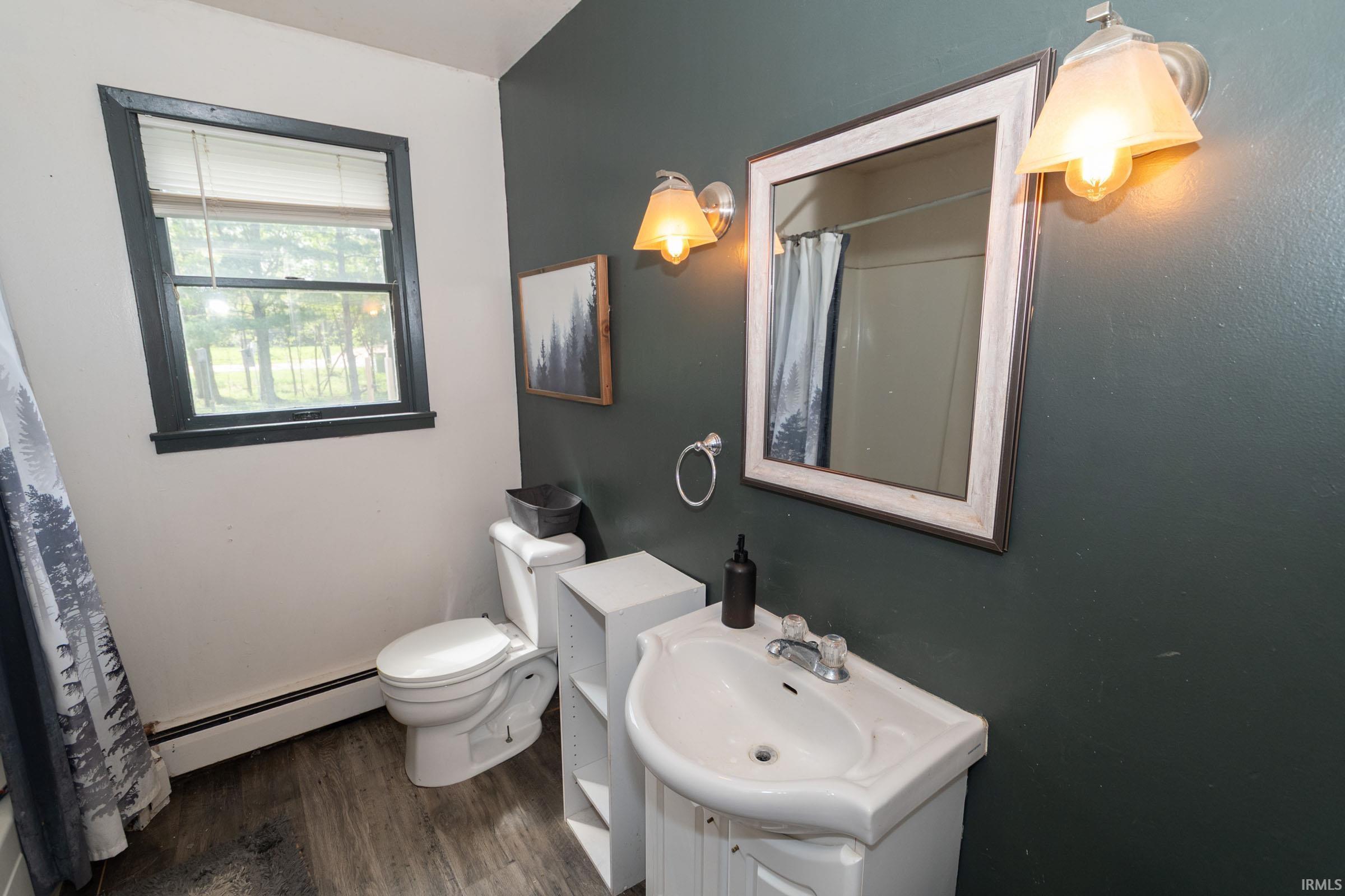 Bathroom featuring wood-finish flooring, a white vanity with an integrated sink, and a framed mirror illuminated by two sconces