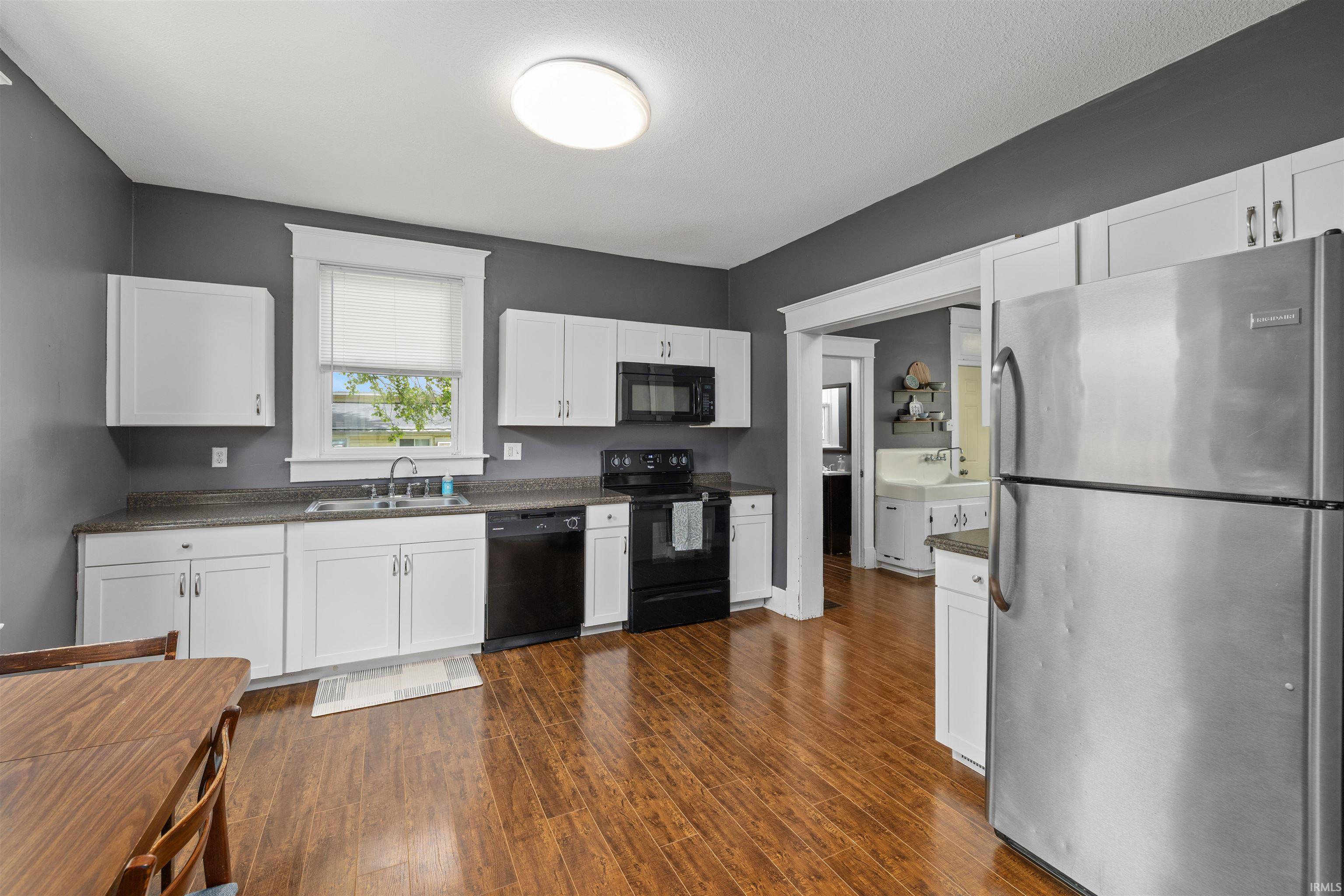 Kitchen featuring wood-finish flooring, white cabinetry, dark countertops, and stainless steel appliances