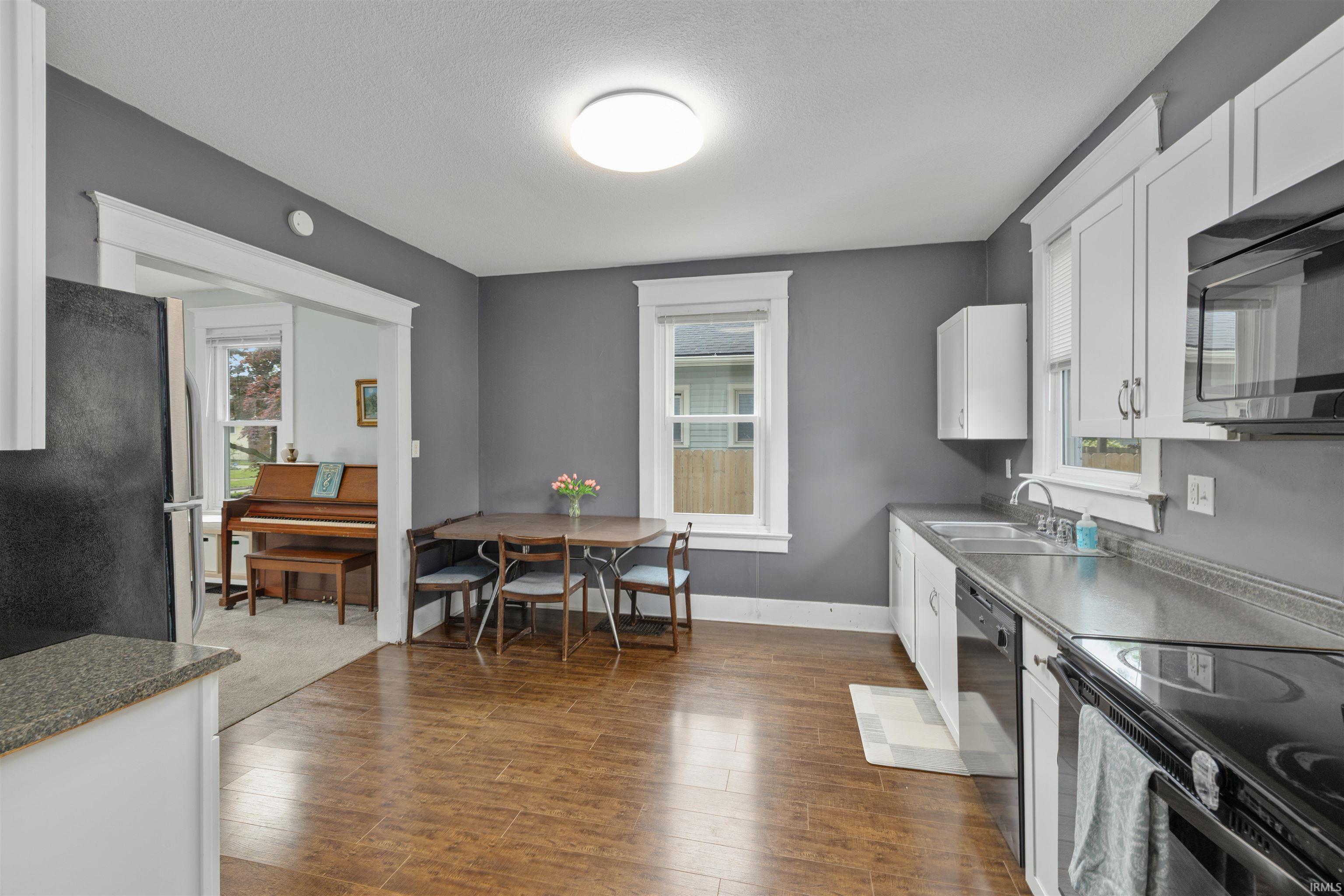 Kitchen featuring wood-finish flooring, white cabinetry, dark countertops, and a full suite of black appliances