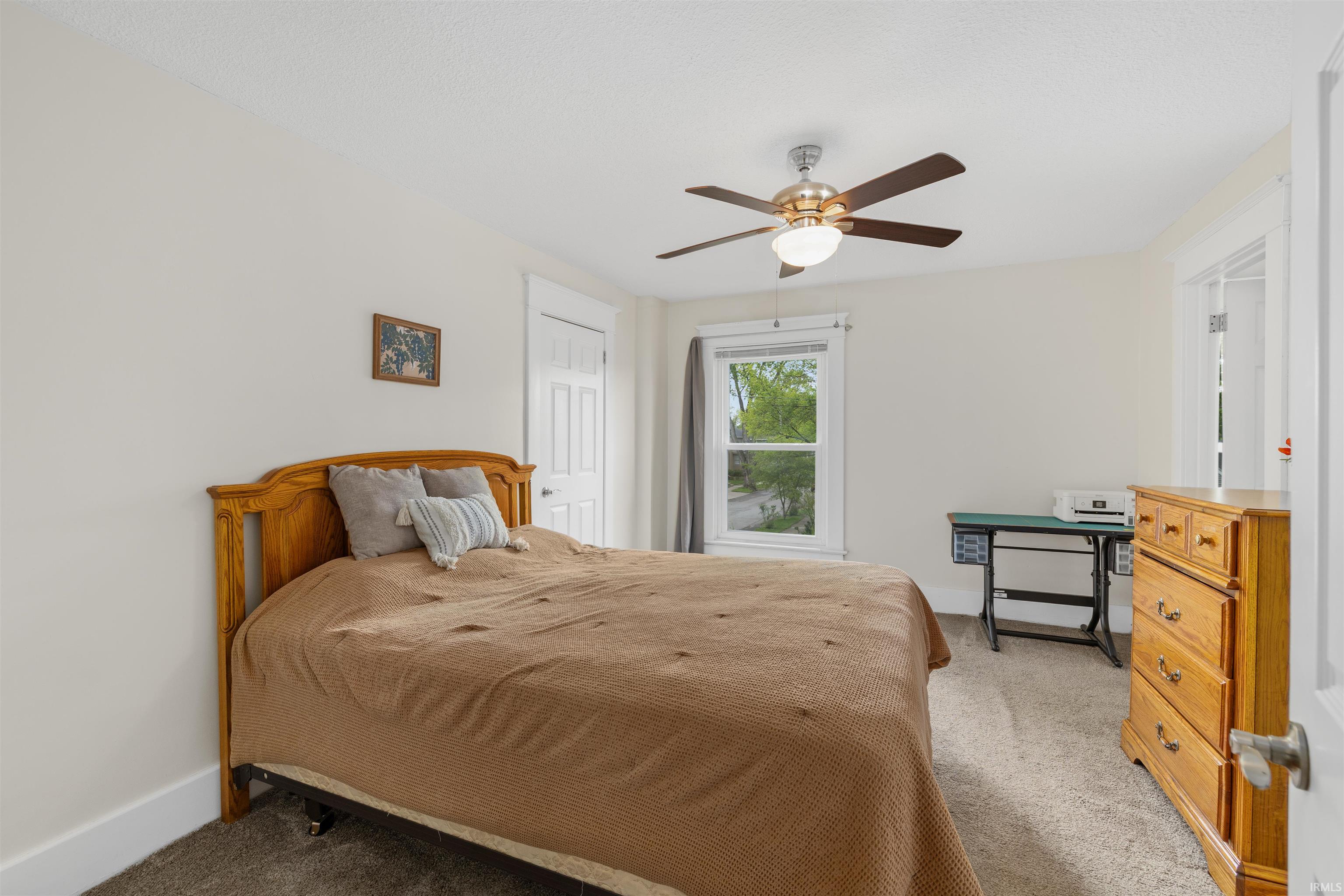 Bedroom featuring light-colored walls, carpet flooring, a window with exterior views, a ceiling fan with integrated lighting, and a white paneled door