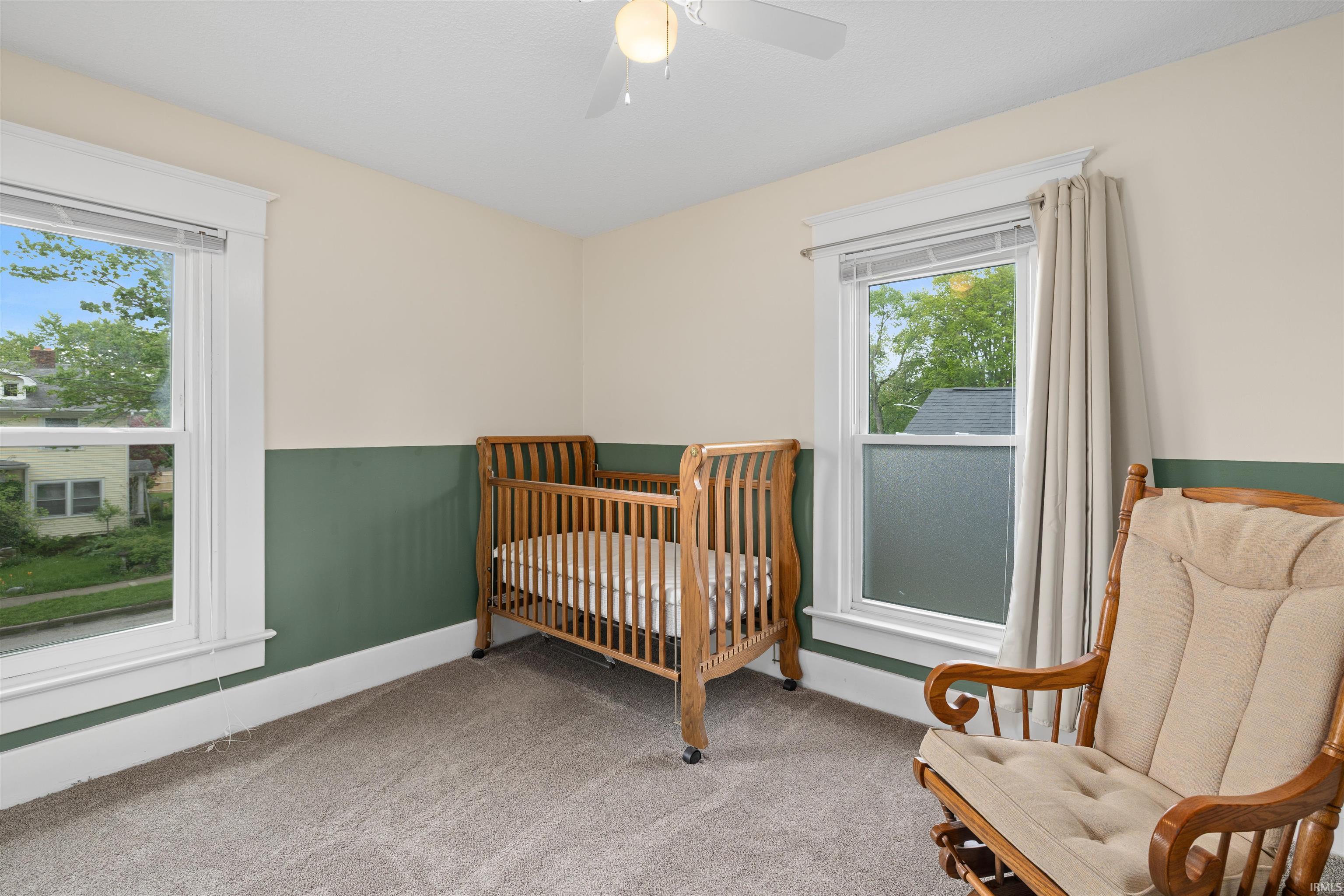 Carpeted room featuring dual windows, two-tone wall paint, a ceiling fan, and white trim
