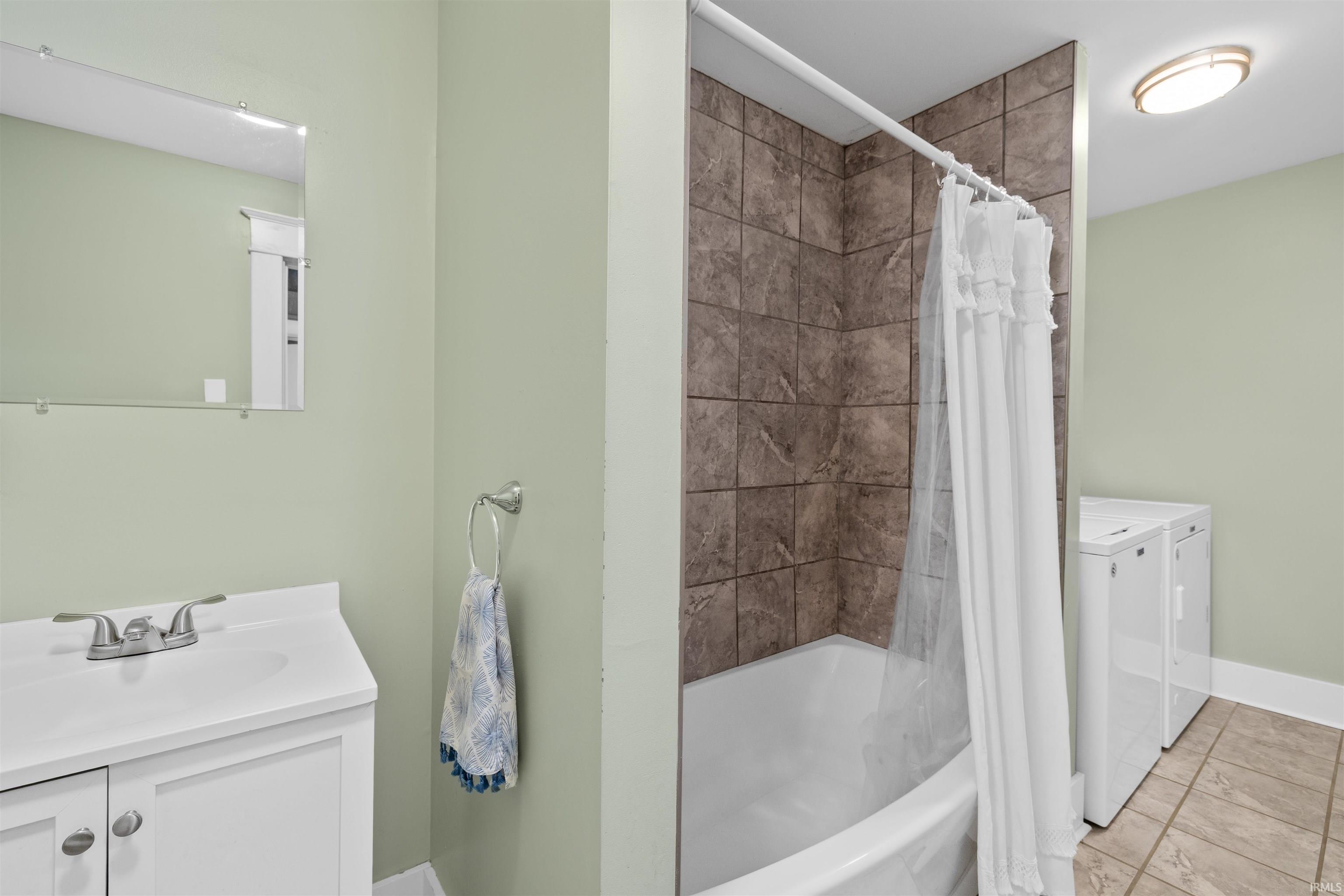 Bathroom featuring a white vanity with a single basin sink, mounted mirror, a tub-shower combination with tiled surround, and integrated laundry appliances