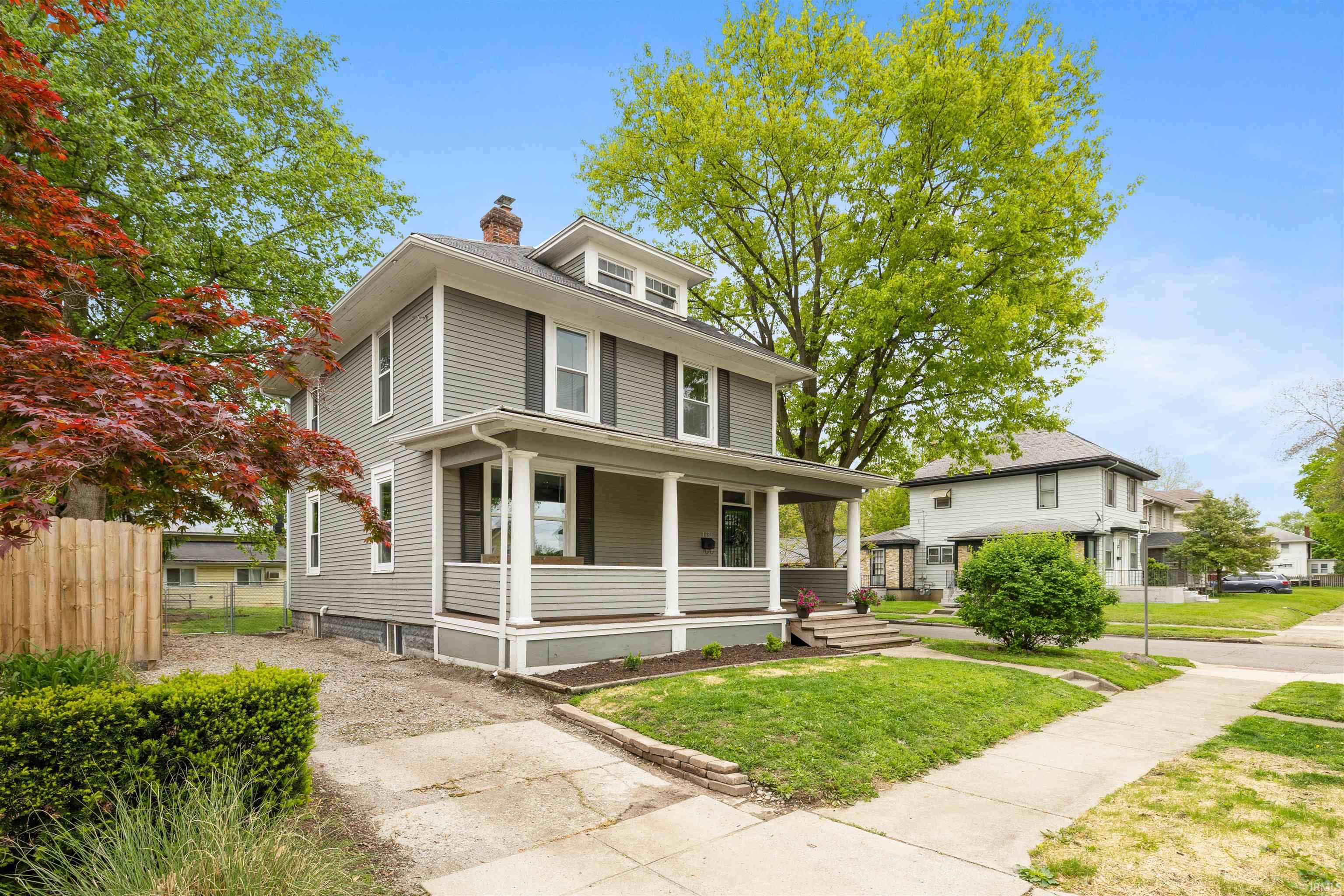 Two-story residence featuring gray siding, a covered front porch with white columns, and dark window shutters