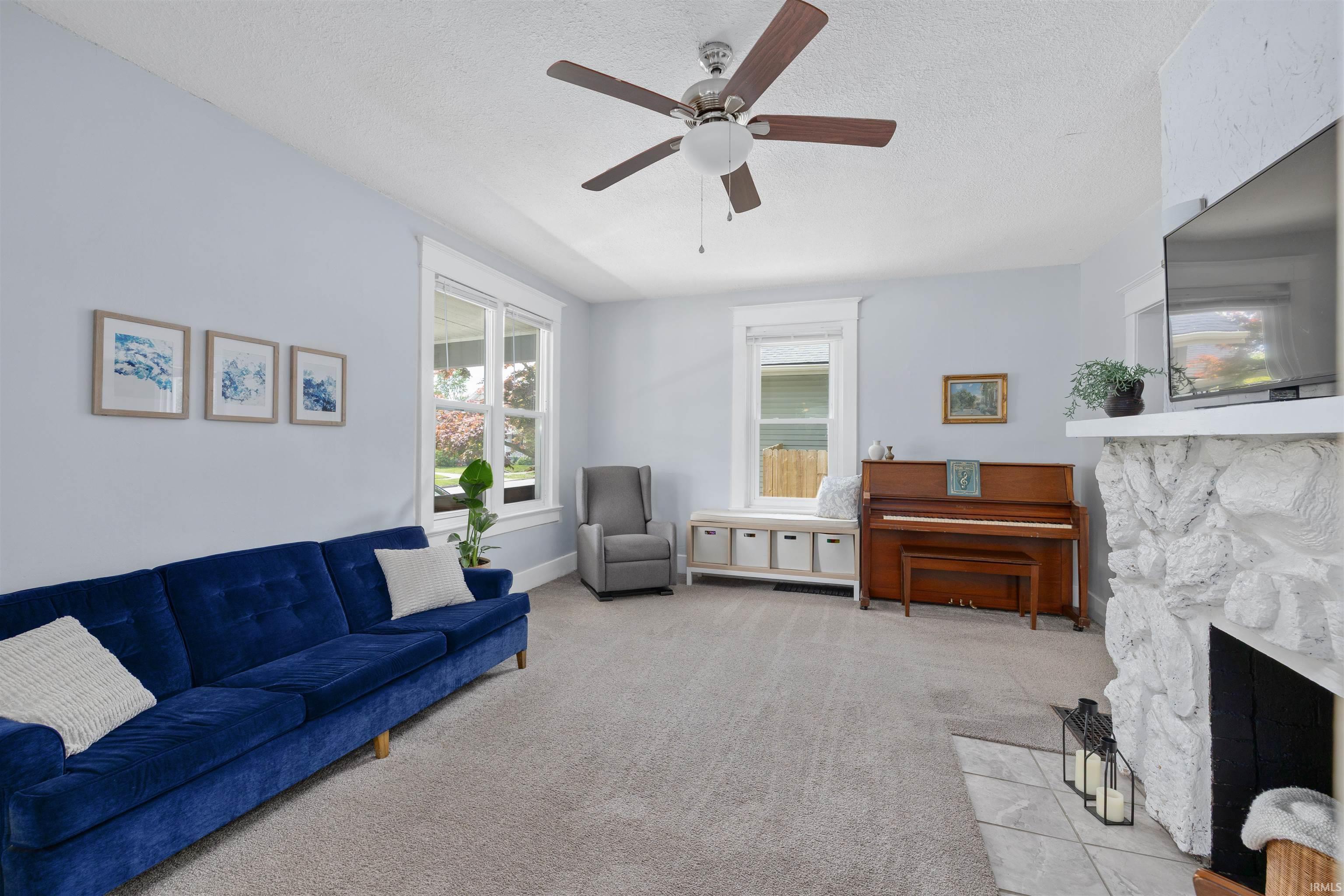 Bright living area featuring light gray carpeting and a white stone fireplace with a tiled hearth