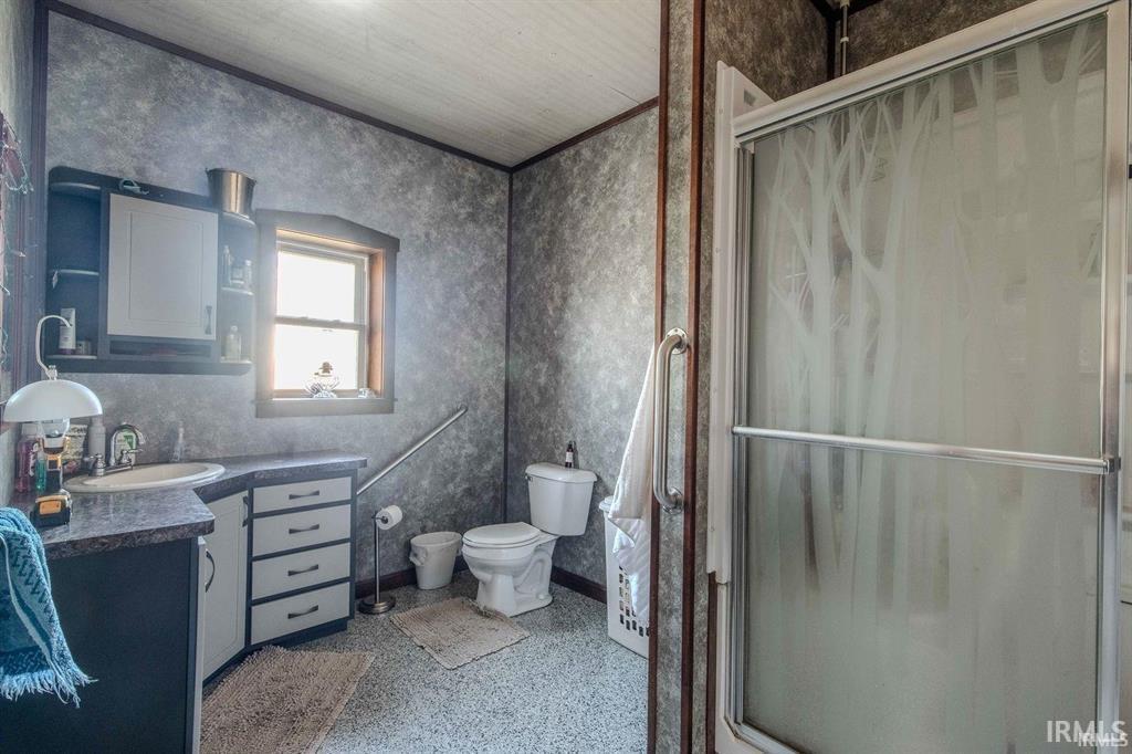 Bathroom featuring a frosted glass shower enclosure with tree-pattern etching, a vanity with a built-in sink and dark countertop, a medicine cabinet with open shelving, a window with wood trim, and textured wall finishes