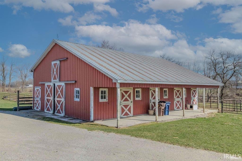 Red barn structure featuring a metal roof, multiple exterior doors with X-brace detailing, a covered porch area, and a gravel drive