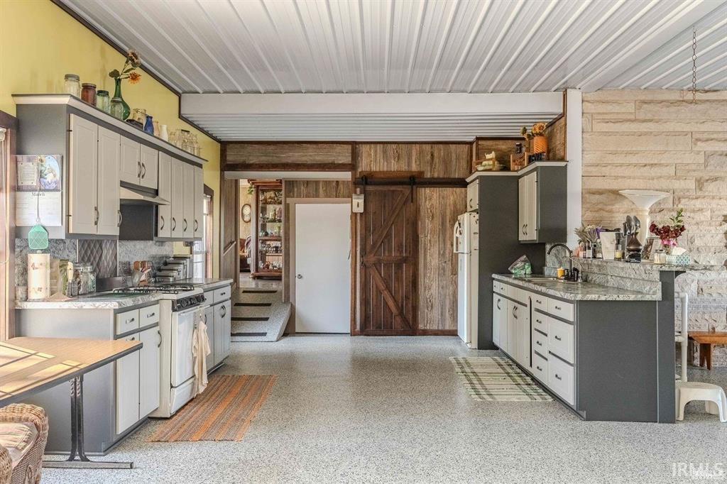 Spacious kitchen featuring an exposed ceiling, built-in cabinetry with light-colored doors and dark frames, light-toned countertops, and a wood-paneled accent wall with a barn door