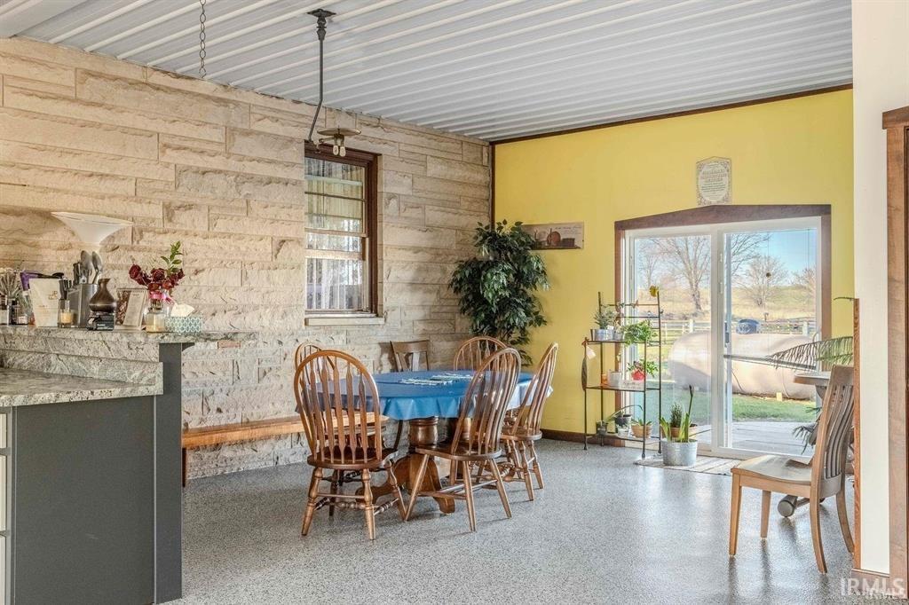 Open-concept room featuring exposed stone walls, a corrugated metal ceiling, and speckled epoxy flooring