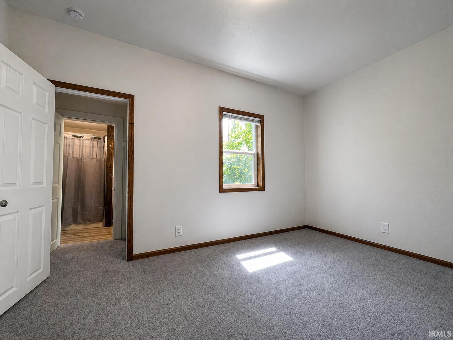 Carpeted room with a single window featuring wood trim