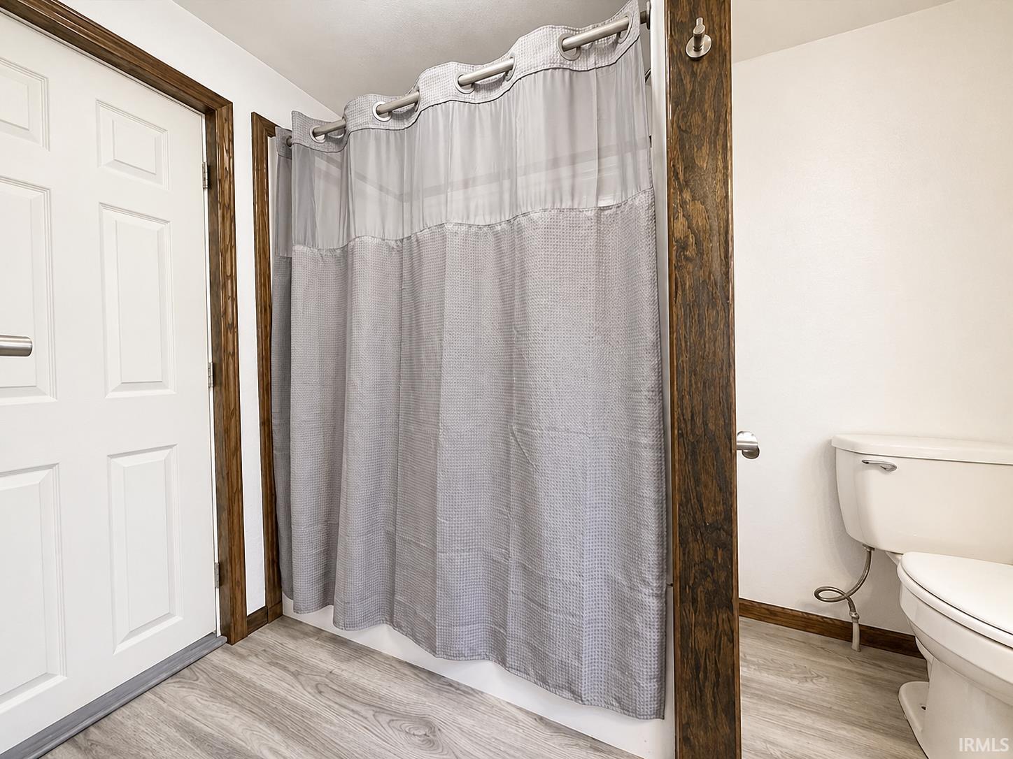 Bathroom featuring wood-finish flooring, a white paneled door with brushed metal hardware, and dark wood-stained trim