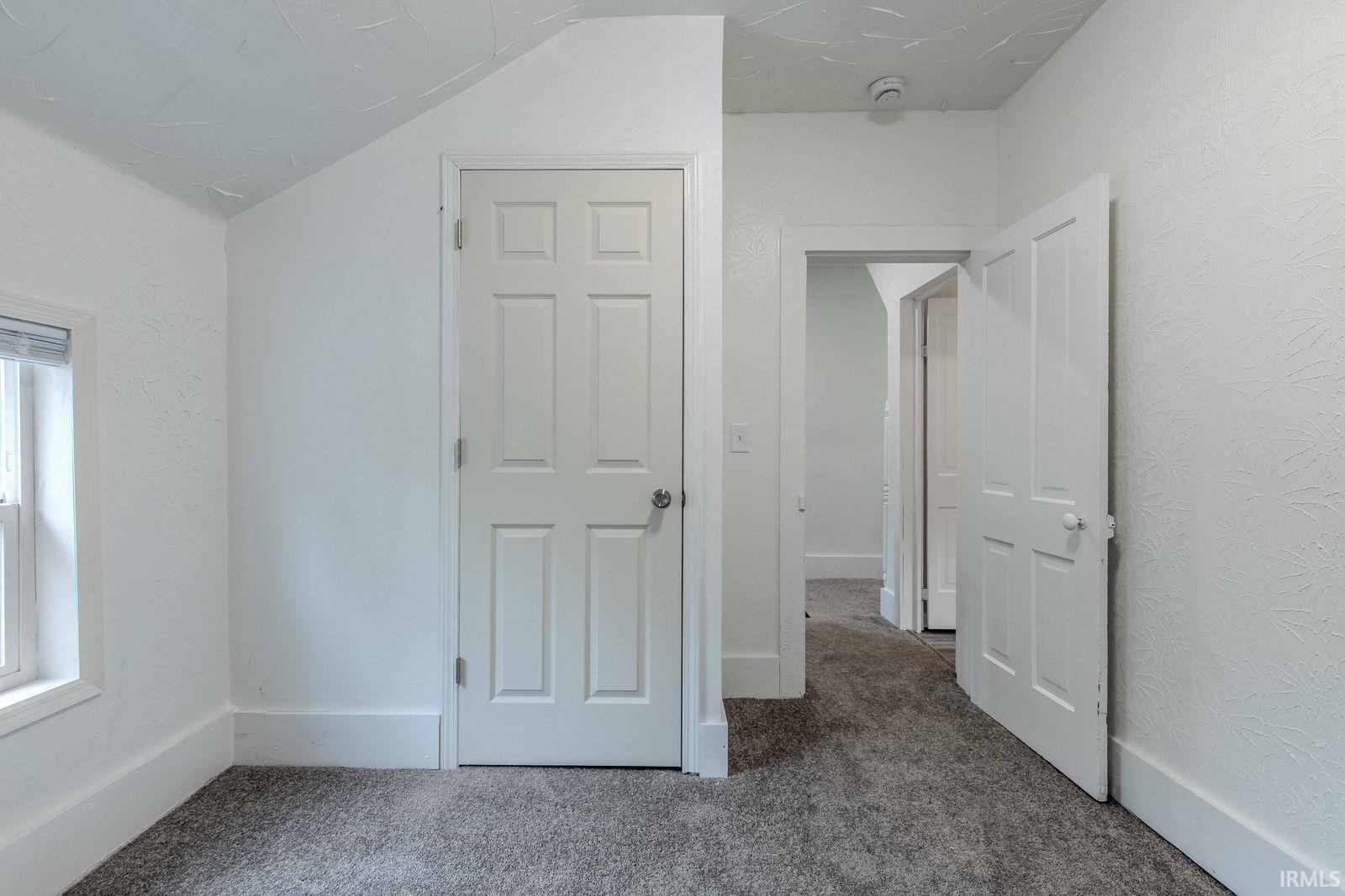 Room featuring gray carpet flooring, white painted walls, white trim, and a white six-panel door