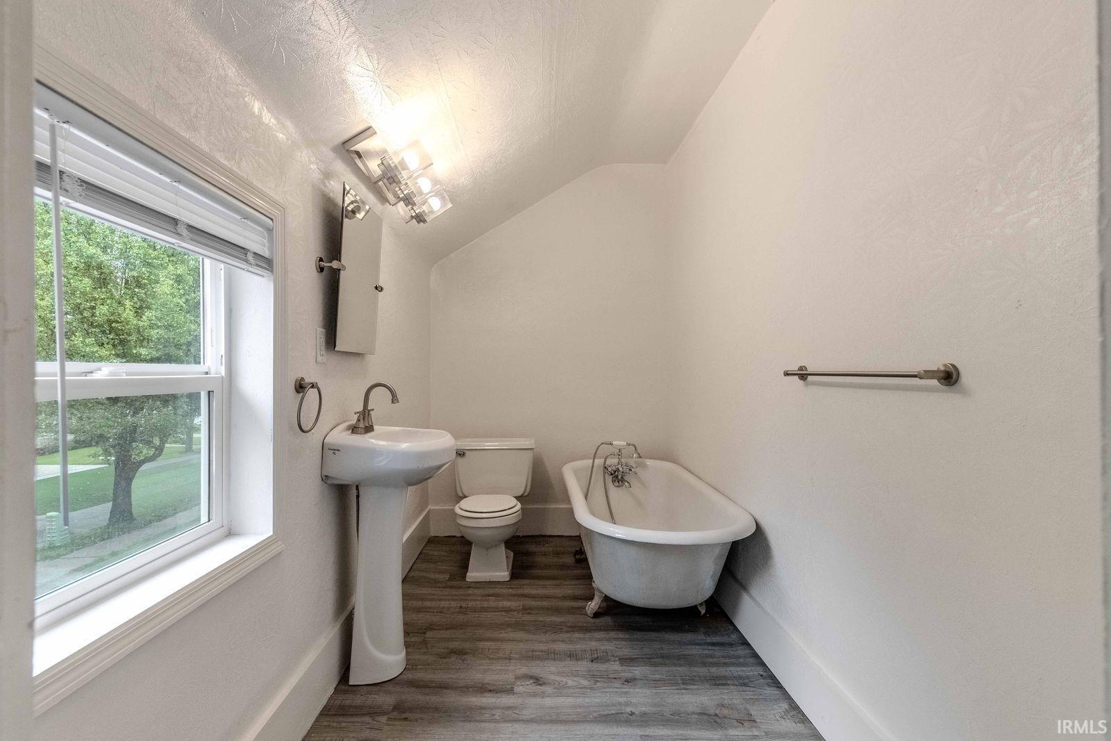 Bathroom featuring a pedestal sink, a clawfoot tub, and wood-finish flooring