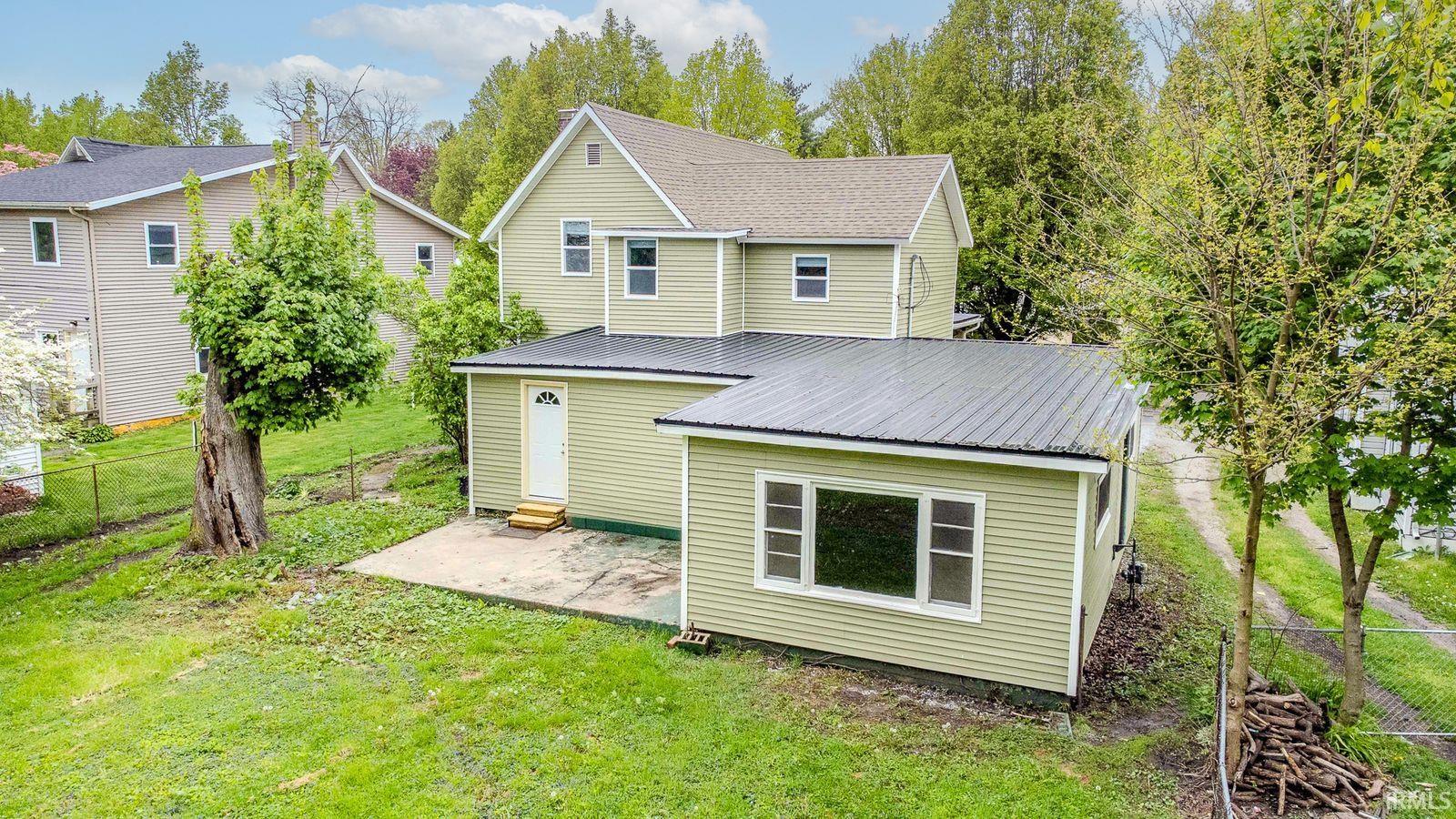 Exterior featuring light green siding, a gabled roof, and an attached extension with a dark metal roof