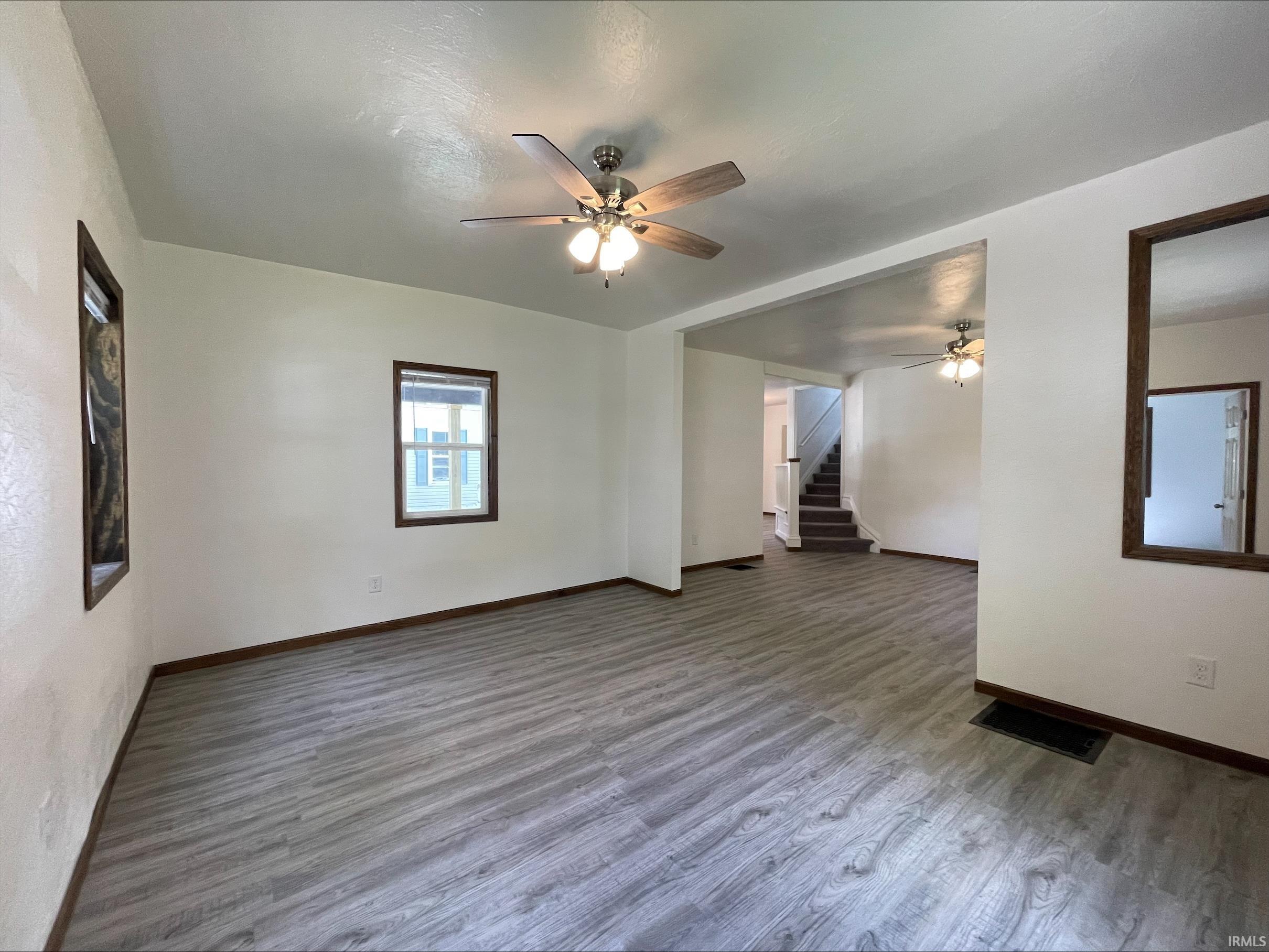 Spacious room featuring gray wood-finish flooring, white walls, and dark wood trim