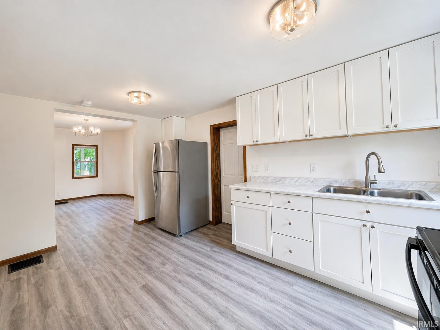 Kitchen featuring white shaker-style cabinetry, a double basin stainless steel sink with a gooseneck faucet, light-toned countertops, and wood-finish flooring