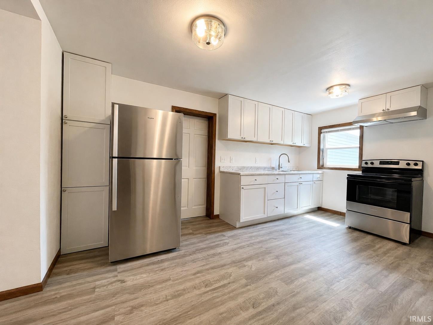 Kitchen featuring wood-finish flooring, white cabinetry, a stainless steel refrigerator, and a stainless steel range with overhead vent